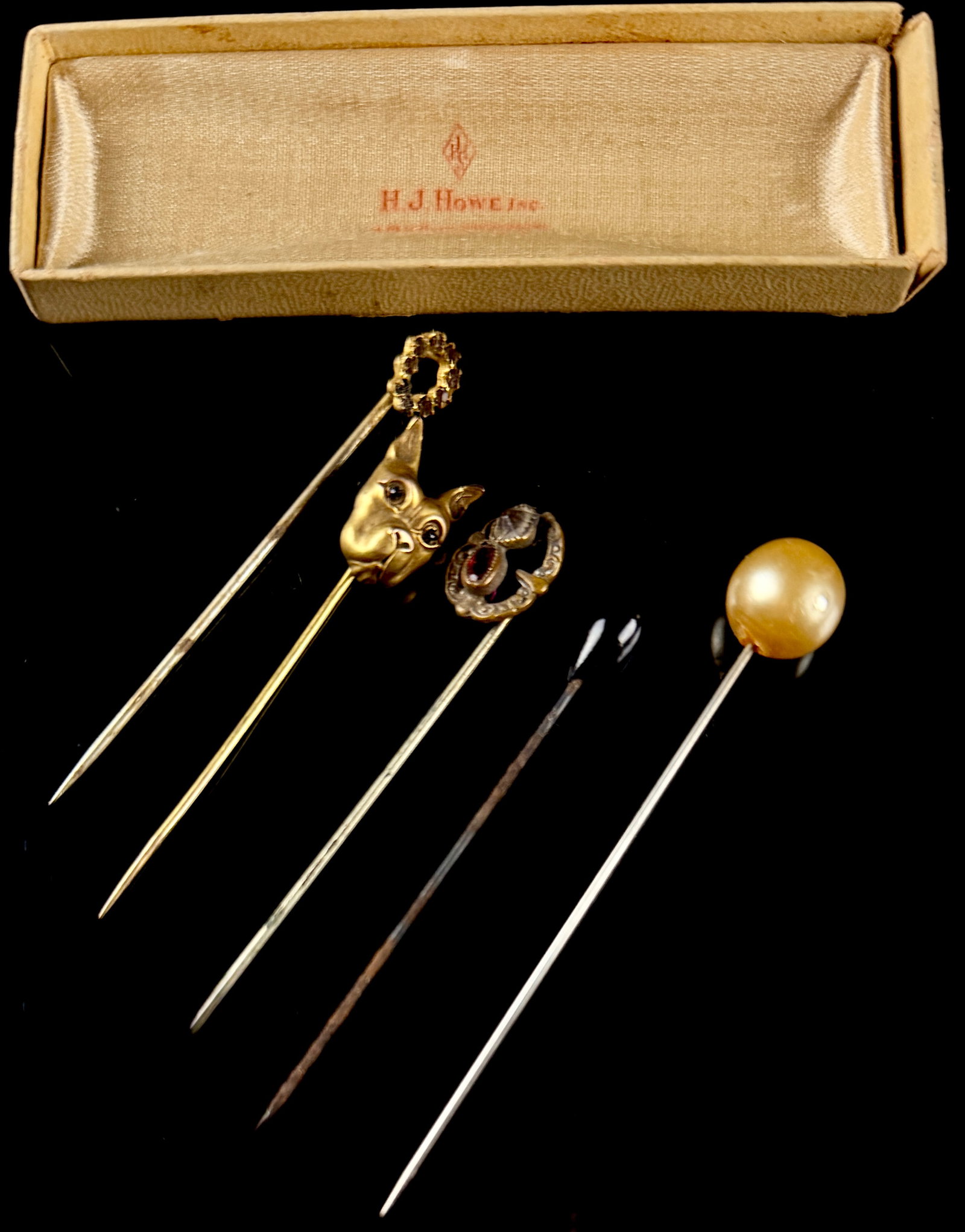 A Set of Five Vintage Gold Toned Stick Pins in H.J. Howe Inc. Presentation Box: A set of five antique and vintage stick pins presented in their original retailer box. The collection features a variety of motifs including a three-dimensional gold-toned dog head pin, likely a bulld