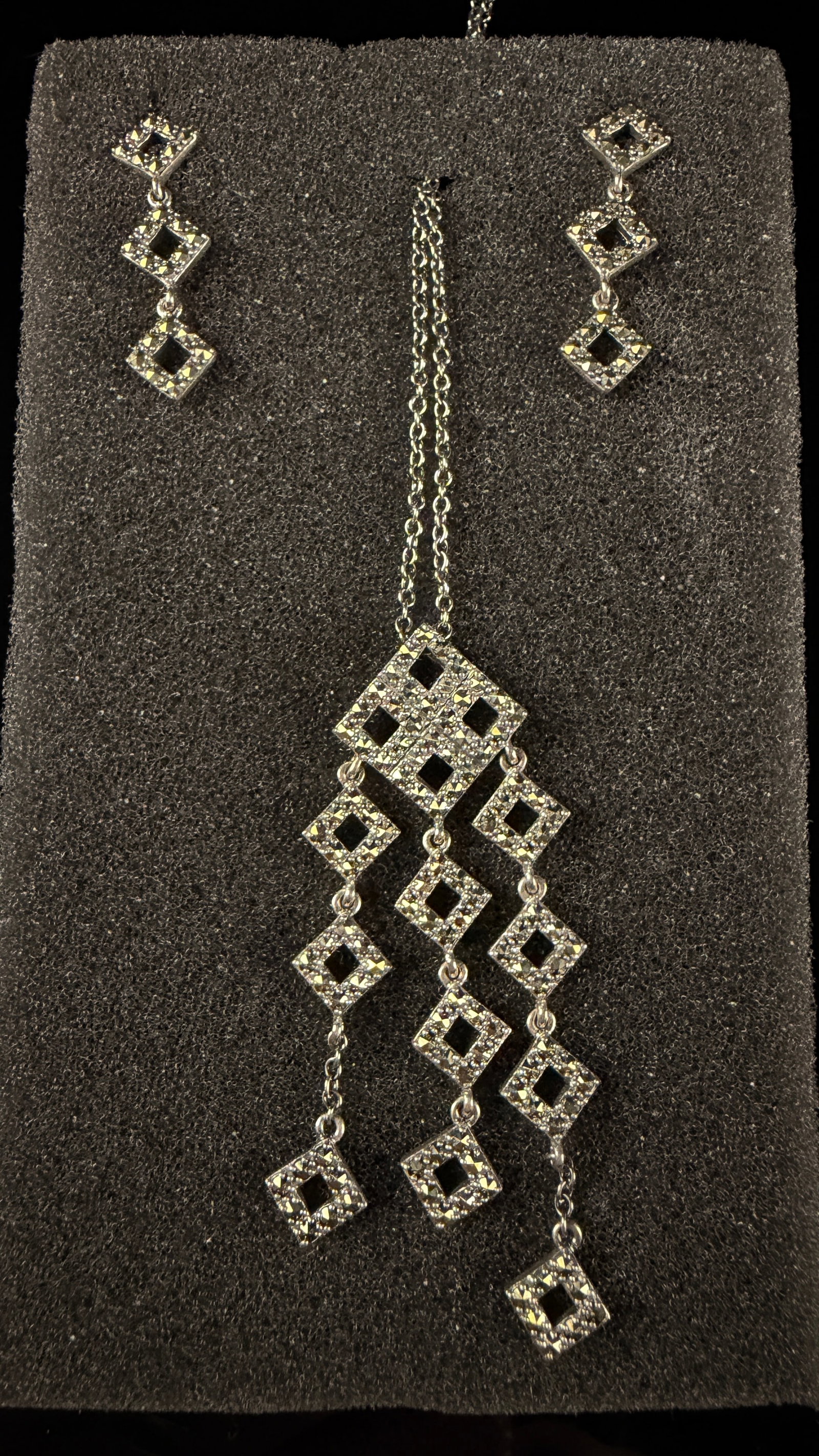 Art Deco Style Sterling Silver and Marcasite Jewelry Set: A jewelry set crafted in sterling silver and marcasite, featuring an Art Deco-inspired geometric design. The set includes a pendant necklace and matching drop earrings constructed with open-work squar