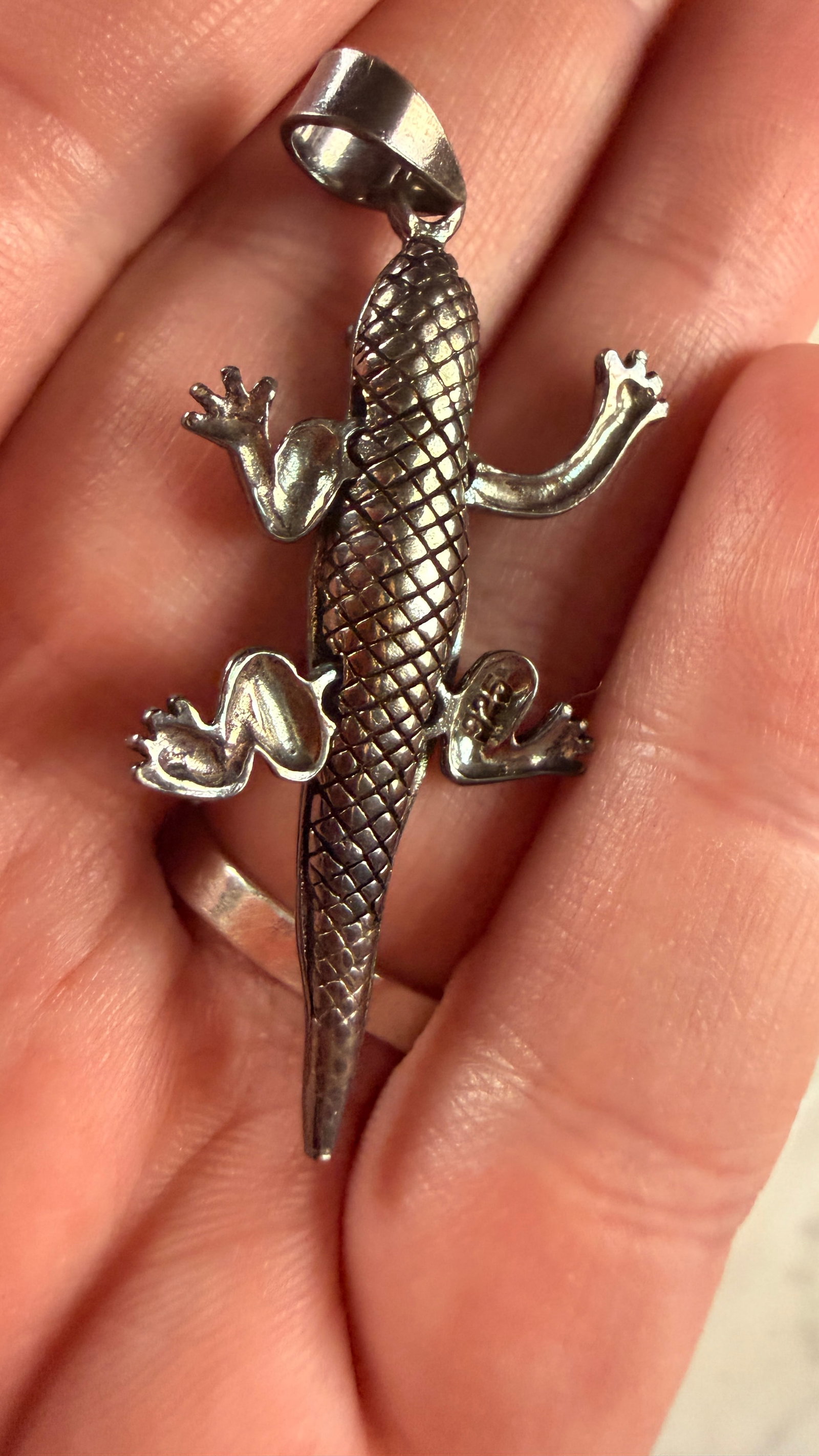 Sterling Silver Movable Gecko Pendant: This sterling silver pendant is designed in the form of a gecko and features movable legs. The body of the lizard is constructed with articulated joints, and the top side is detailed with a textured c