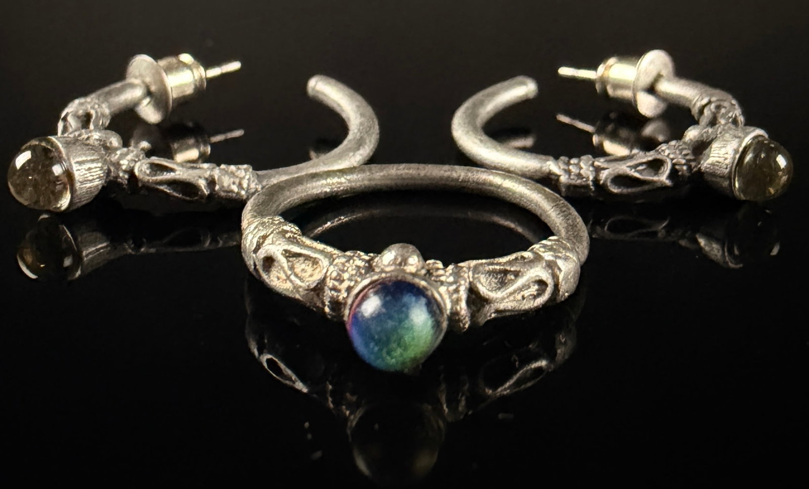A Trio of Artisan Silver-Toned Jewelry Pieces with Iridescent Cabochons: A trio of artisan jewelry consisting of a ring and a pair of coordinating open-hoop stud earrings. The pieces are crafted in an unmarked silver-toned metal with a textured, antiqued finish. Each item 