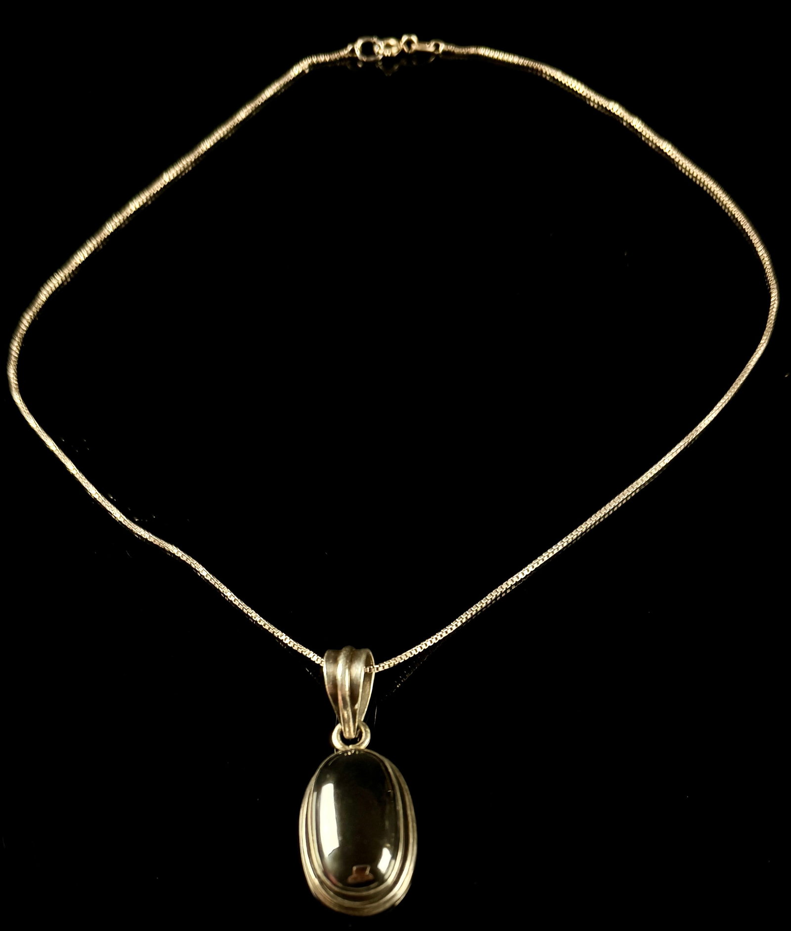 Sterling Silver and Black Cabochon Pendant Necklace: This sterling silver pendant necklace features a polished black gemstone cabochon, displaying a high-shine, metallic luster consistent with hematite. The oval stone is held in a smooth bezel setting