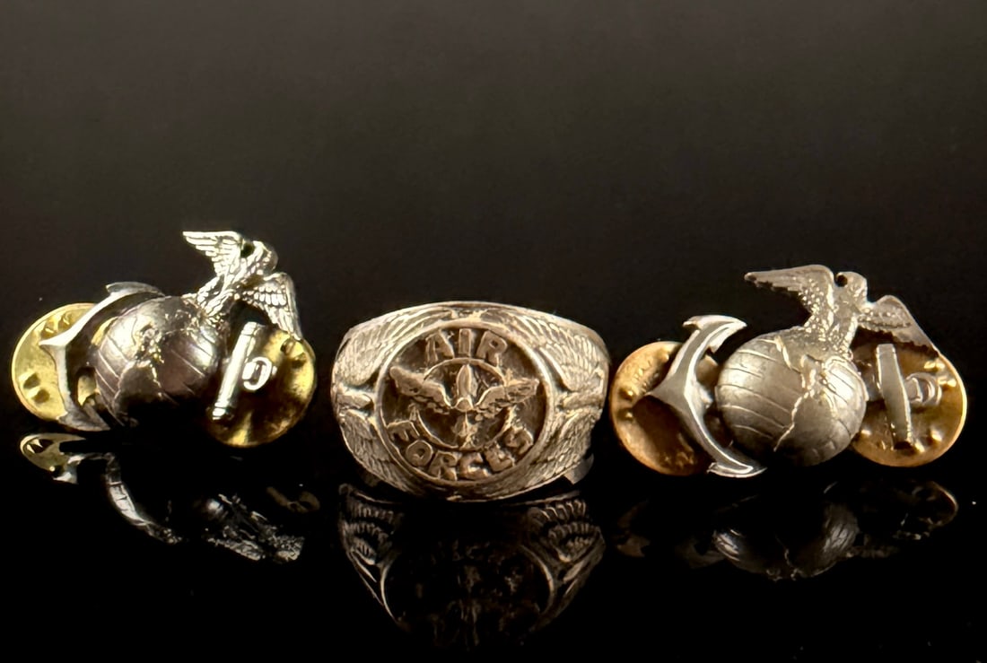 A Trio of US Military Memorabilia comprising a USAAF Service Ring and USMC Insignia Pins: This lot consists of a US Army Air Forces (USAAF) service ring and a pair of United States Marine Corps (USMC) insignia pins. The ring is a cast metal commemorative piece, likely dating to the World W