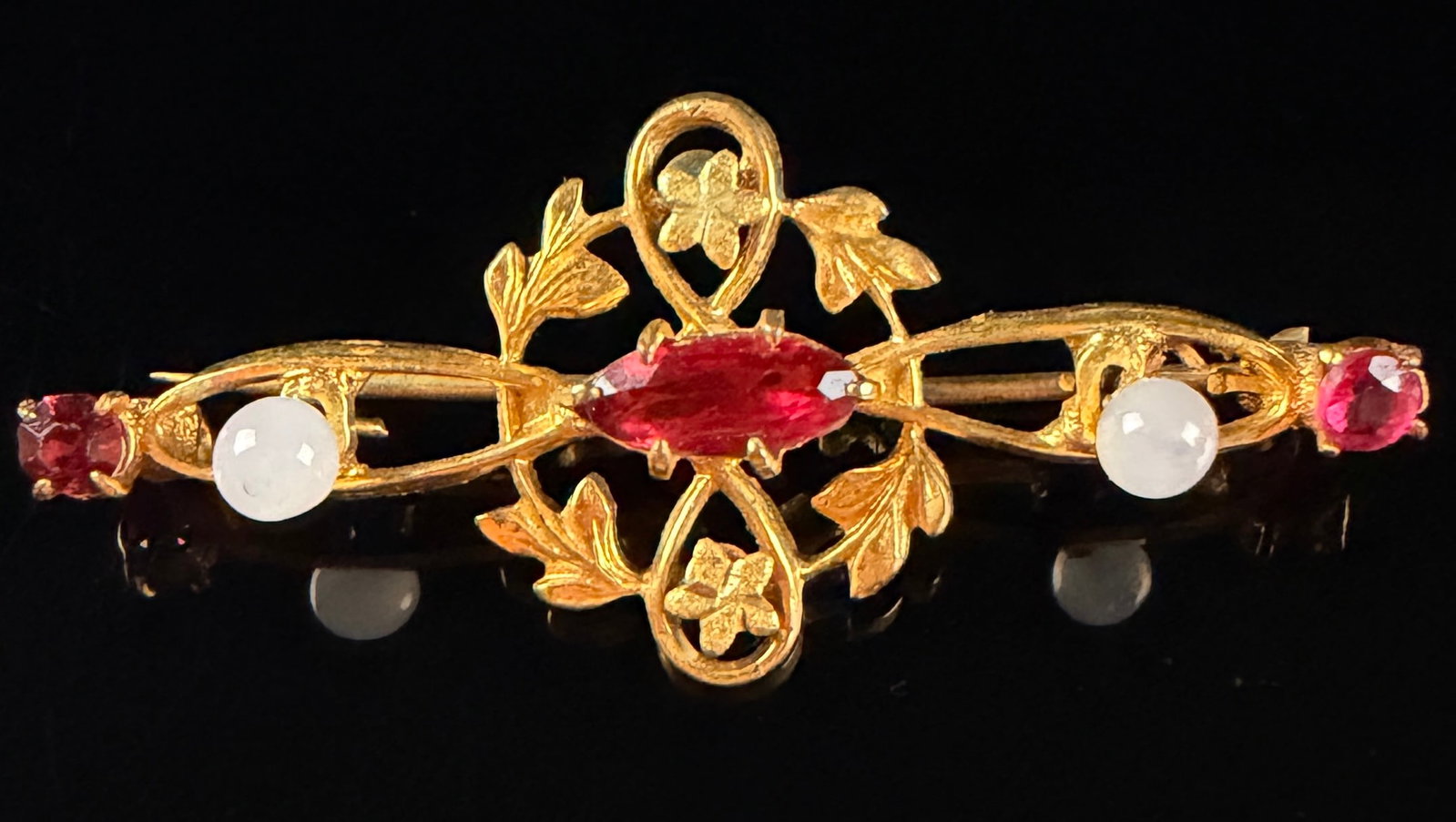 Late Victorian Yellow Gold Floral Openwork Bar Brooch with Red and White Gemstones: Late Victorian or early Edwardian era bar brooch featuring a stylized foliate and floral openwork motif. The central design is set with a marquise-cut red gemstone, likely a garnet or ruby, flanked