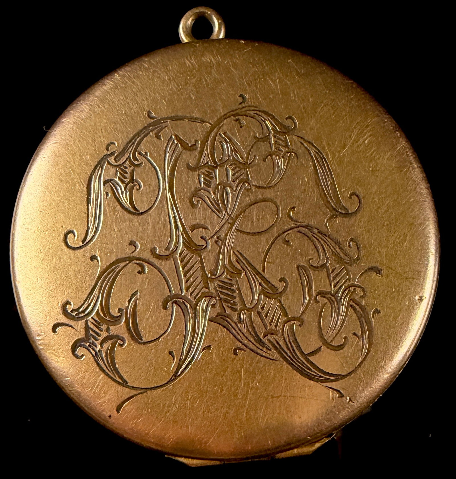 Antique Yellow-Tone Metal Hinged Locket with Engraved Monogram and Dated 1902: This circular yellow-tone metal locket features a hinged design with internal compartments for two photographs. The front face is decorated with a hand-engraved foliate monogram in an ornate script. T
