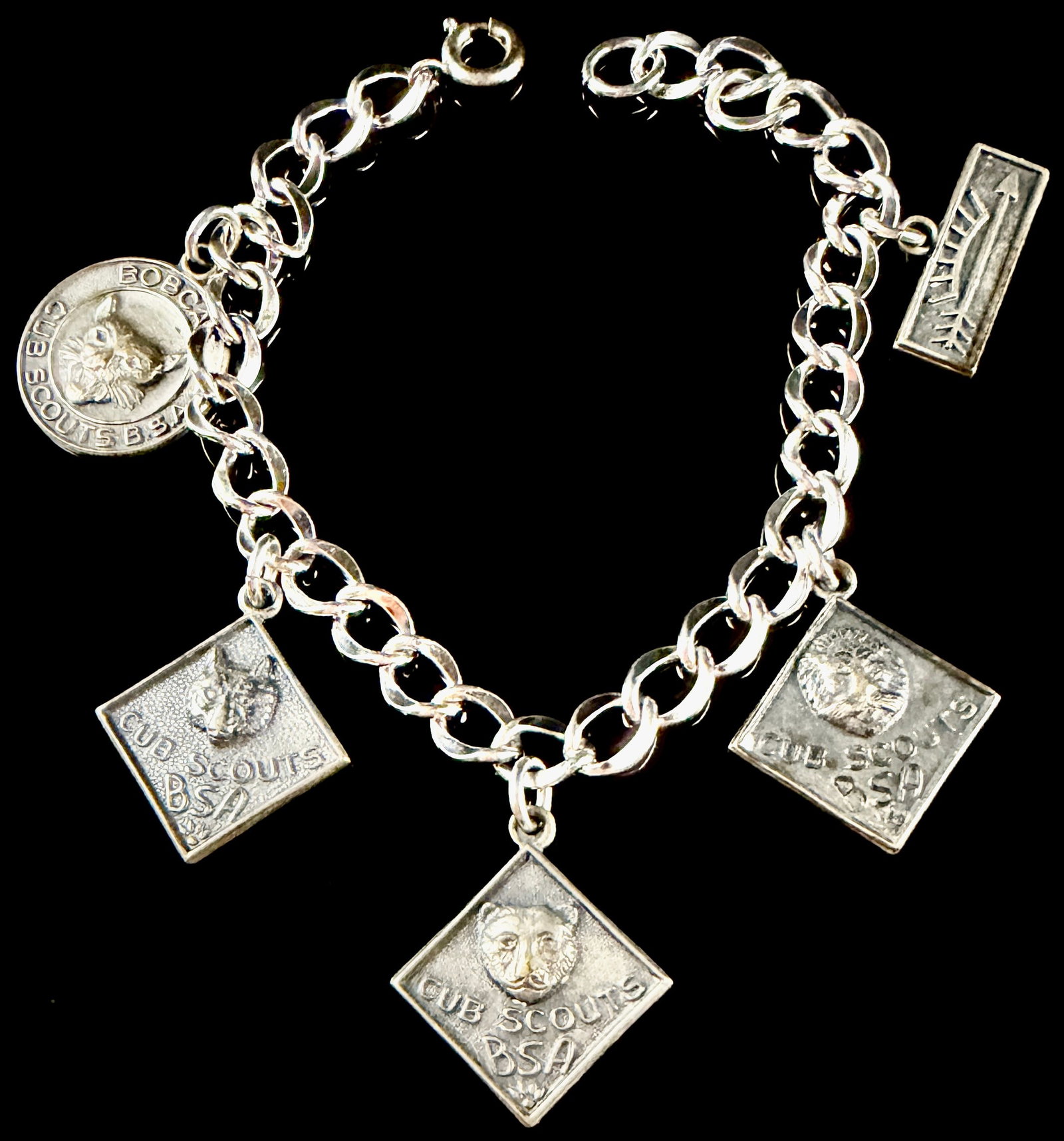 Vintage Cub Scout Sterling Silver Charm Bracelet: This vintage sterling silver charm bracelet commemorates the ranks and achievements within the Boy Scouts of America Cub Scout program. The jewelry piece features a heavy curb link chain supporting fi