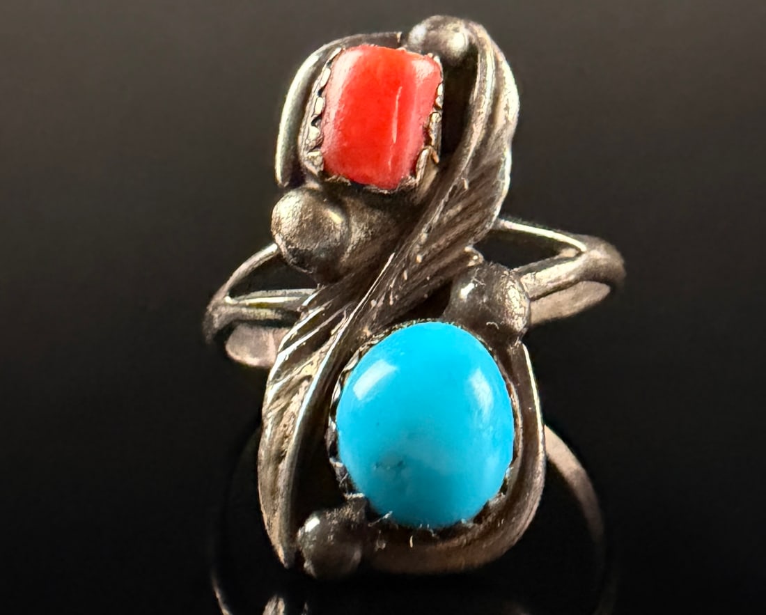 Navajo Running Bear Trading Co Sterling Silver Turquoise and Coral Bypass Ring: A vintage Southwestern bypass cocktail ring crafted in sterling silver. The design features two cabochon stones: one rectangular red coral and one oval bright blue turquoise, each set within a sawtoot