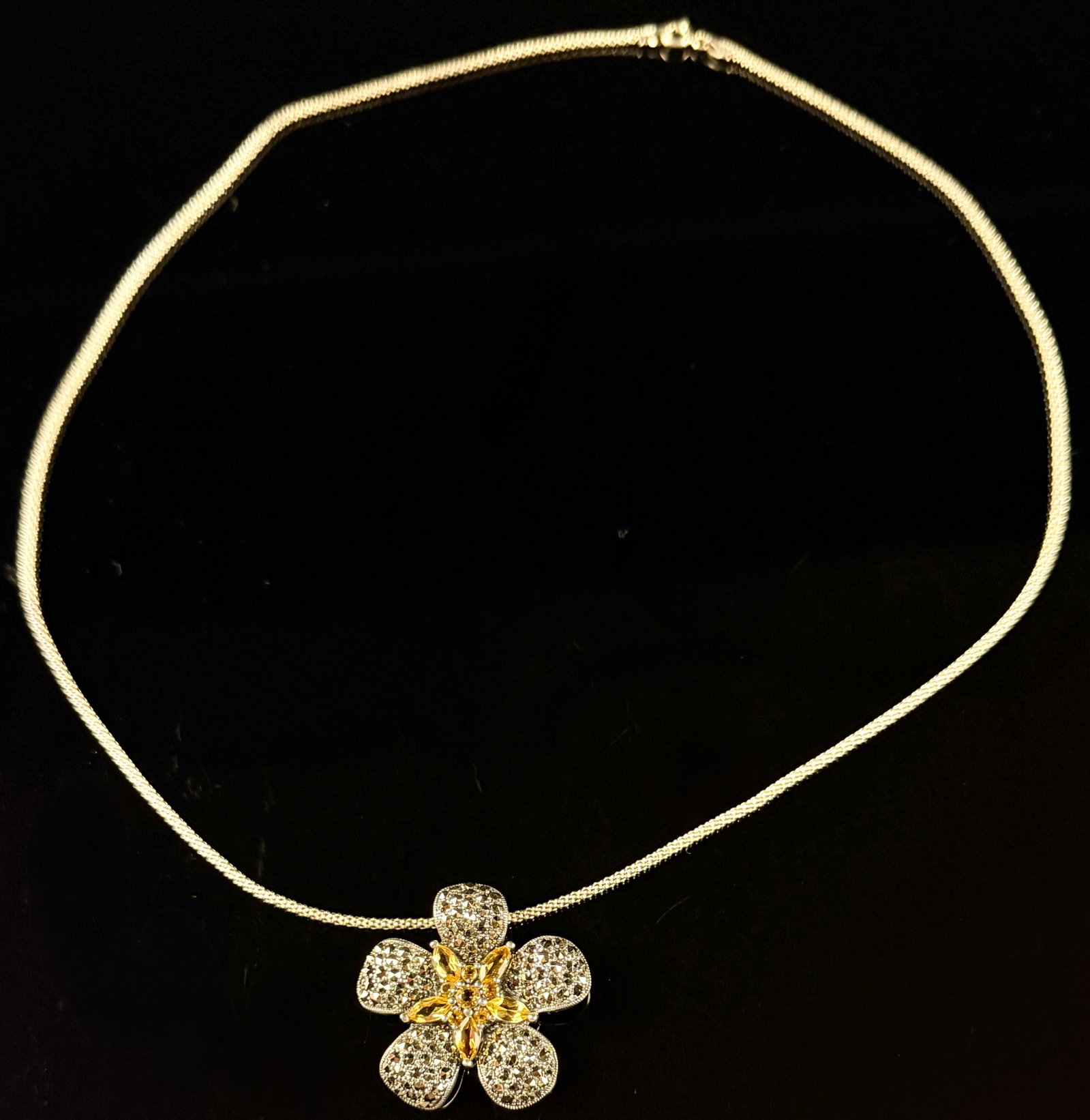 Sterling Silver Marcasite and Yellow Citrine Flower Pendant Necklace: This jewelry item is a sterling silver pendant necklace featuring a five-petal floral design. The outer petals of the pendant are pav?-set with numerous faceted metallic-grey stones, identifying as ma