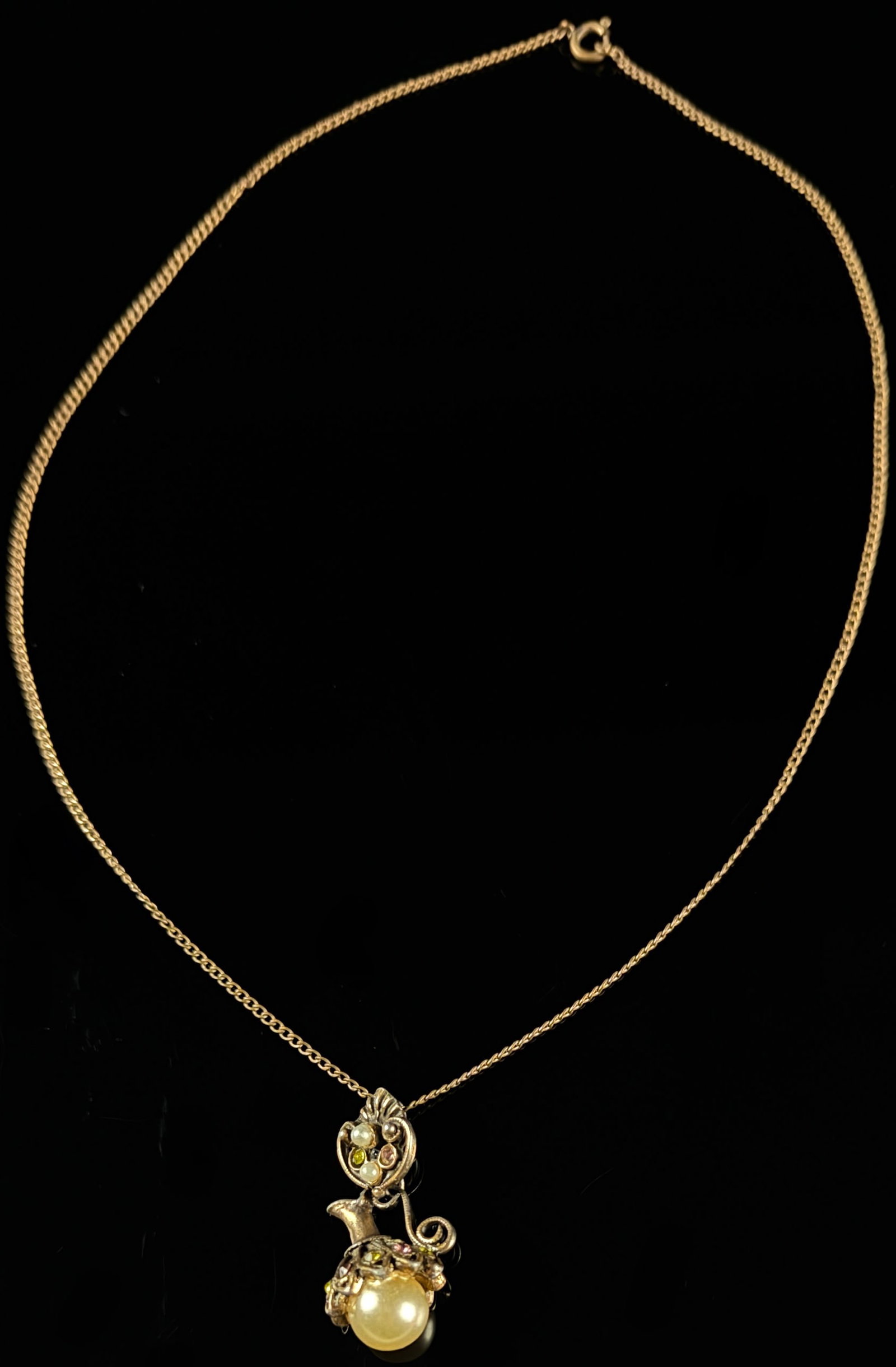 Vintage Gold Tone Miniature Ewer Novelty Pendant Necklace with Faux Pearls and Colored Stones: This vintage costume jewelry pendant necklace features a novelty motif in the shape of a miniature ewer or pitcher. The pendant is crafted from gold-tone metal and is composed of two articulated secti