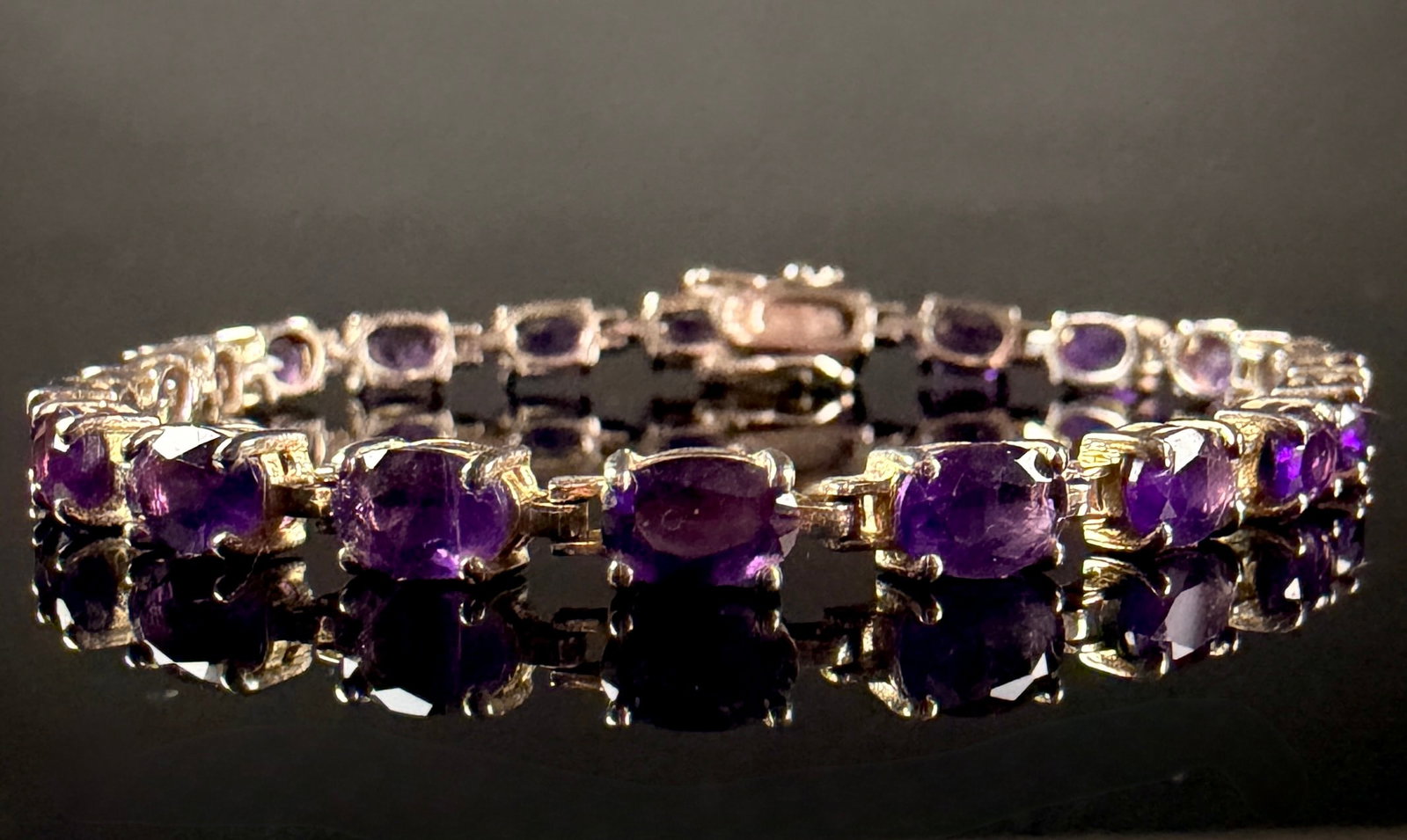 Sterling Silver and Oval-Cut Amethyst Tennis Bracelet: This tennis link bracelet is crafted from sterling silver and features twenty-four oval-cut faceted amethysts. Each gemstone is individually set in a four-prong mounting. The stones exhibit a deep,