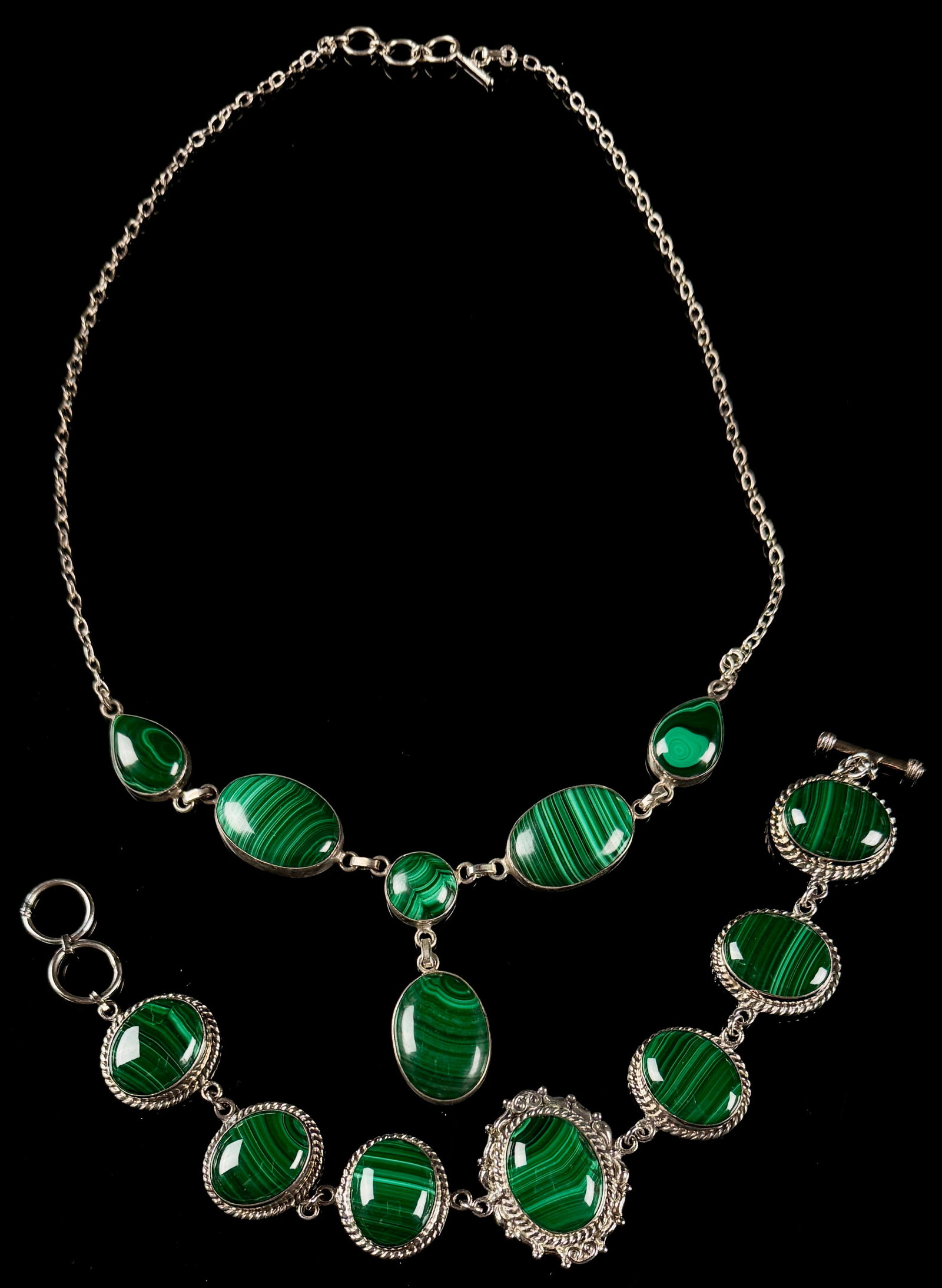 A Pair of Sterling Silver and Malachite Jewelry Items: This jewelry set consists of a necklace and a bracelet, both featuring polished green banded cabochons that appear to be malachite. The gemstones are bezel-set in sterling silver. The necklace is
