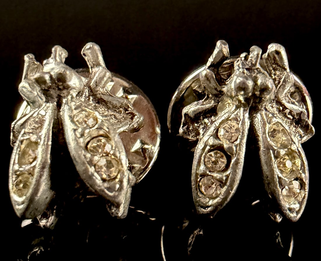 A Pair of Silver-Toned Insect Motif Rhinestone Set Lapel Pins: A pair of silver-toned lapel pins or tie tacks designed in the form of stylized insects, resembling bees or flies. The pieces are cast from a silver-toned metal with textured bodies and outstretched w