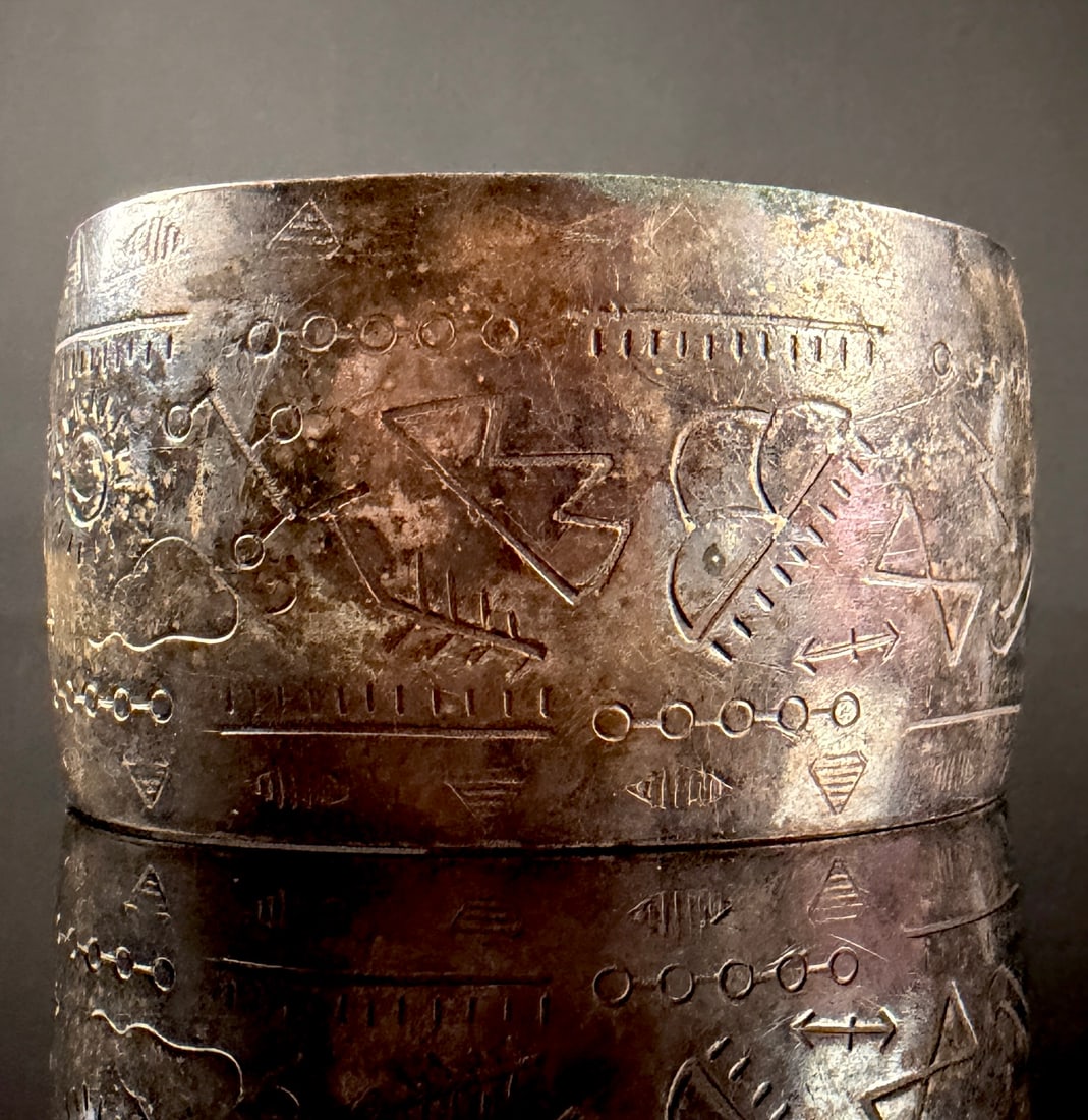 Vintage Southwestern Style Silver Plated Copper Pictograph Cuff Bracelet: A vintage wide cuff bracelet featuring a series of etched and stamped Southwestern style pictograph motifs. The decorative elements include a sun, clouds with rain, lightning bolts, crossed arrows, a 