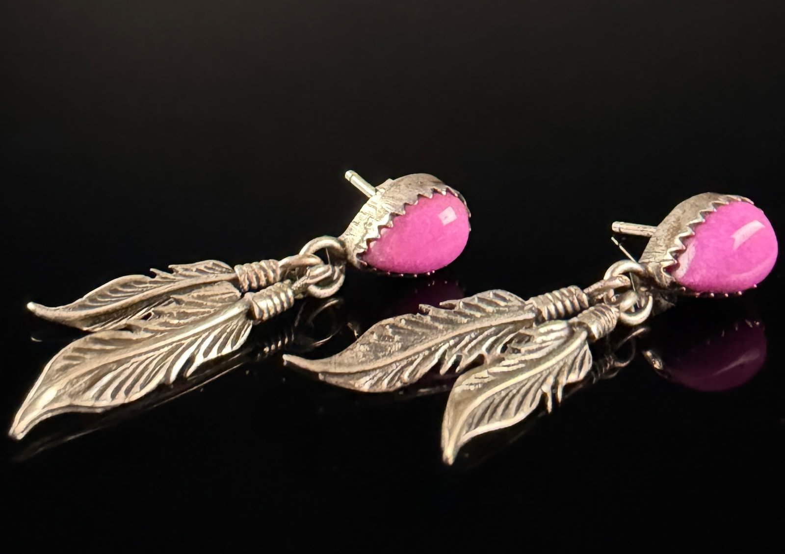 A Pair of Navajo Style Sterling Silver and Pink Cabochon Feather Drop Earrings: A matched pair of Southwestern-style drop earrings, featuring design elements attributed to Navajo silversmith Richard Begay. Each earring is centered by a teardrop-shaped vibrant pink cabochon, secur