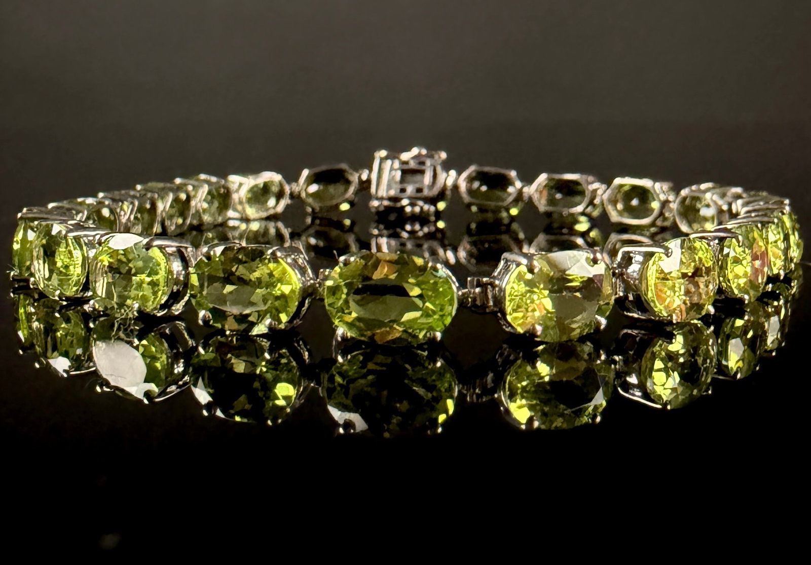 Sterling Silver and Oval Cut Peridot Tennis Bracelet: This sterling silver tennis-style link bracelet features a continuous row of oval-cut peridots. The jewelry consists of twenty-five individual gemstones, each secured in a classic four-prong setting. 