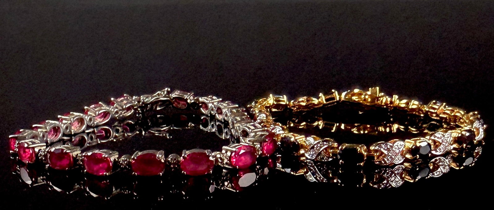 Two Gemstone-Set Tennis Bracelets in Sterling Silver and Gold-Tone Metal: This lot features two gemstone-set tennis bracelets. The first is a sterling silver link bracelet featuring seventeen oval faceted red gemstones, each held in a four-prong setting. The underside of th