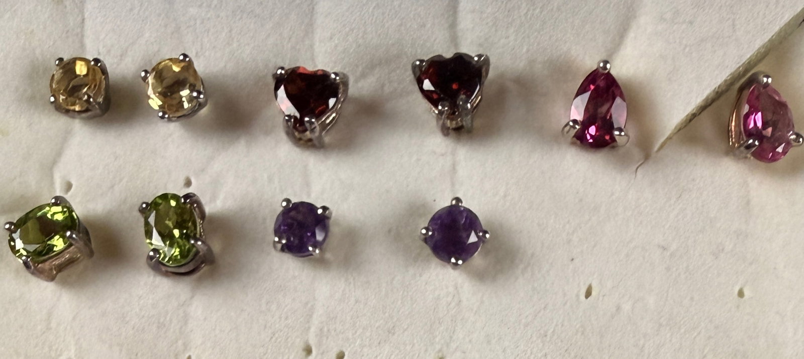 An Assortment of Sterling Silver and Mixed Gemstone Stud Earrings: This assortment of jewelry features multiple pairs of faceted gemstone stud earrings prong-set in sterling silver. The collection includes round-cut purple stones that appear to be amethyst, oval-cut 