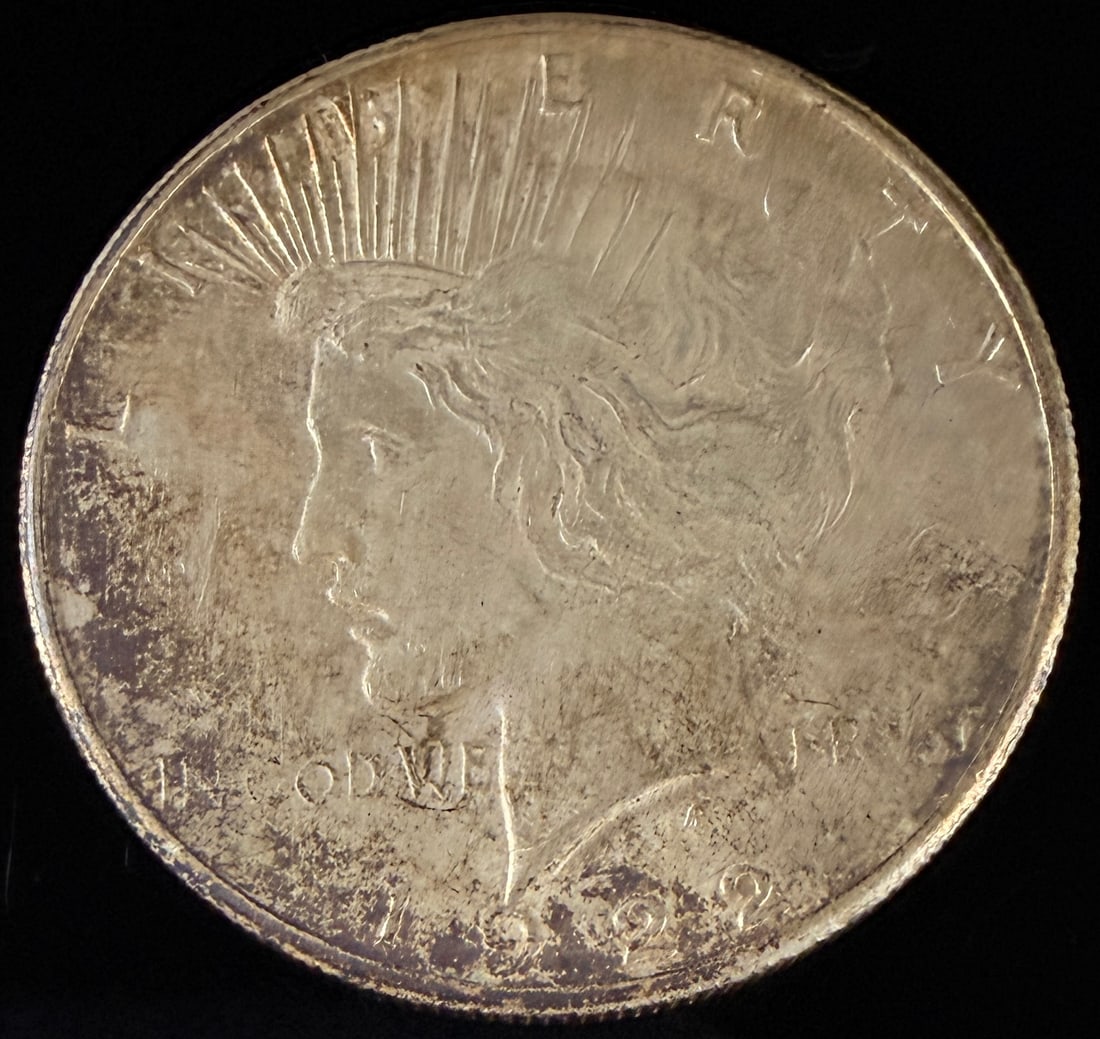 1922 US Peace Silver Dollar, Philadelphia Mint: A 1922 US Peace silver dollar struck at the Philadelphia Mint. The coin features the Liberty head obverse and the eagle reverse. It is composed of 90% silver and 10% copper. The piece has a reeded edg