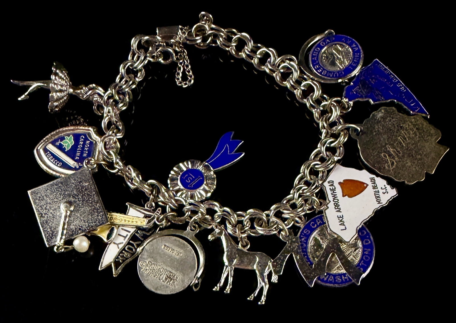 Mid-20th Century Sterling Silver Jacoby-Bender Charm Bracelet with 13 Enamel and Figural Charms: A vintage sterling silver double-link charm bracelet featuring an assortment of thirteen travel-themed and commemorative charms. The bracelet is fitted with a fold-over box clasp manufactured by Jacob