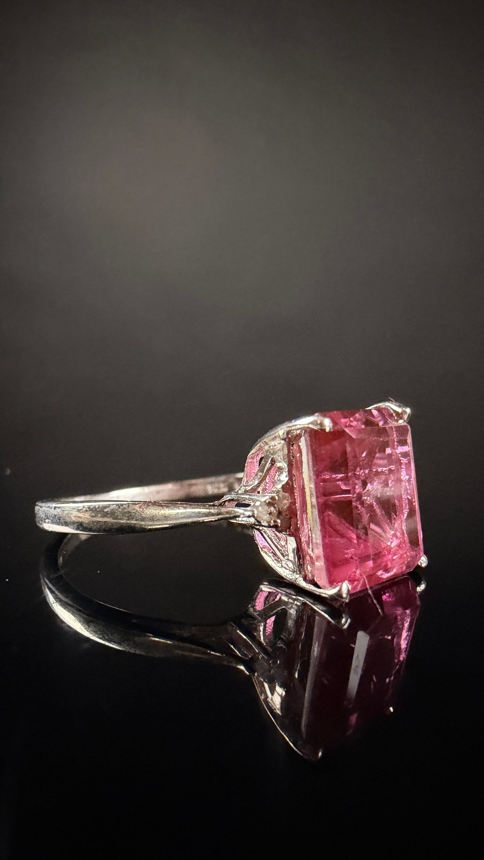 Sterling Silver Cocktail Ring with Emerald Cut Pink Gemstone and Colorless Accents: A sterling silver cocktail ring featuring a large emerald-cut pink gemstone. The centerpiece is held in a four-prong mount within an openwork decorative basket. The pink gemstone displays visible inte