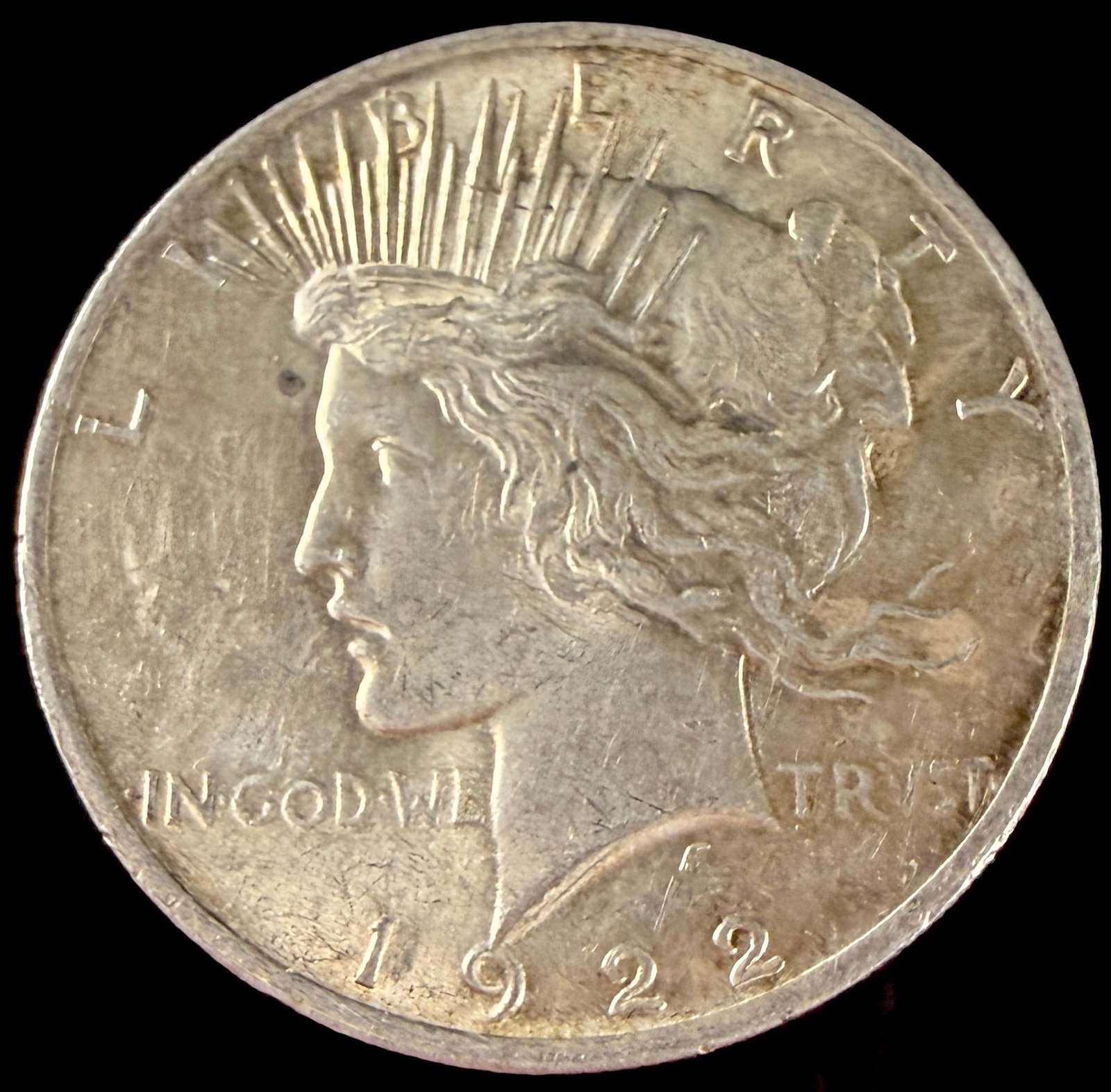 1922 US Peace Silver Dollar: US 1922 Peace silver dollar struck at the Philadelphia Mint. The coin is composed of 90 percent silver and 10 percent copper. The obverse features the Liberty head design with a radiate crown, and the