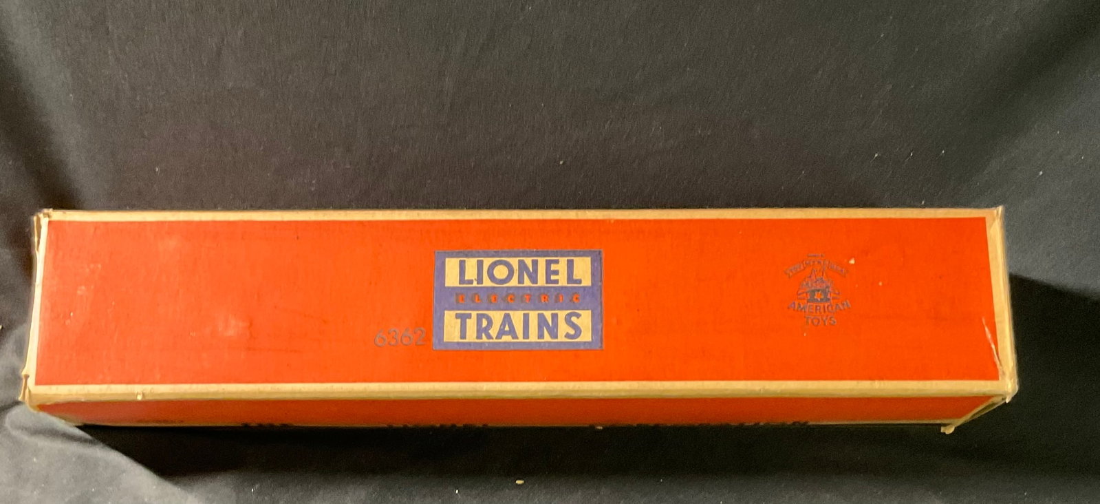 Lionel O-Gauge No. 6362 Rail Truck Car with Original Box: A vintage Lionel O-gauge rail truck flatcar, catalog number 6362. The car features a molded orange plastic body mounted on a black metal frame. It carries a removable load consisting of three railroad