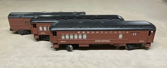 A Trio of Pennsylvania Railroad O-Gauge Passenger Cars: A trio of O-gauge model train passenger cars in the livery of the Pennsylvania Railroad, attributed to Lionel. The lot includes three distinct car types: a Railway Post Office (RPO) car numbered 9510 