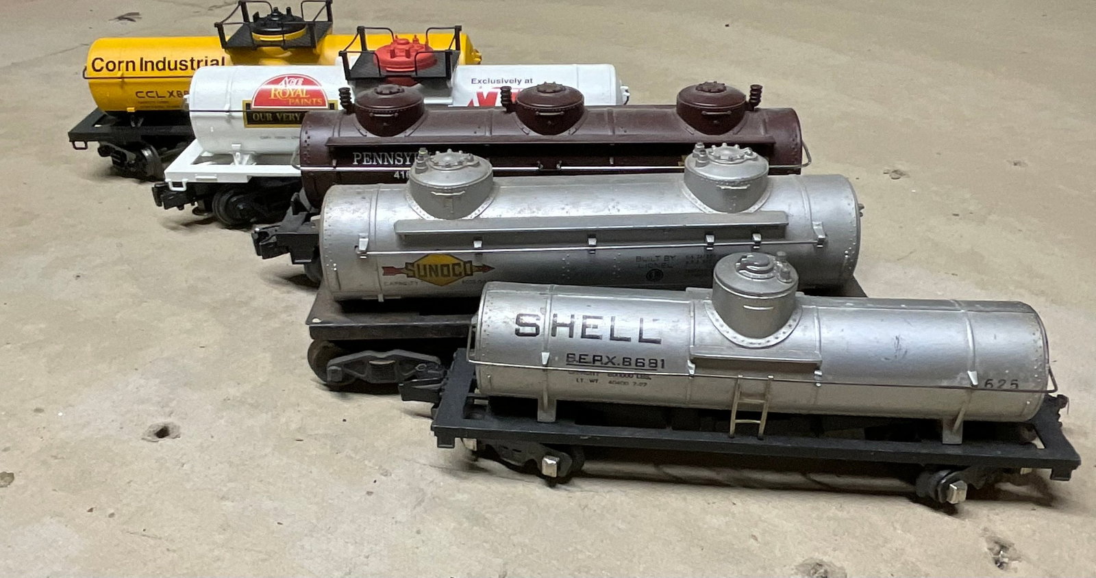 A Group of Five Lionel O Gauge Tank Cars including Shell and Sunoco Examples: A group of five O gauge model train tank cars featuring a mix of vintage postwar and modern era rolling stock primarily manufactured by Lionel. The collection includes several distinct models: a silve