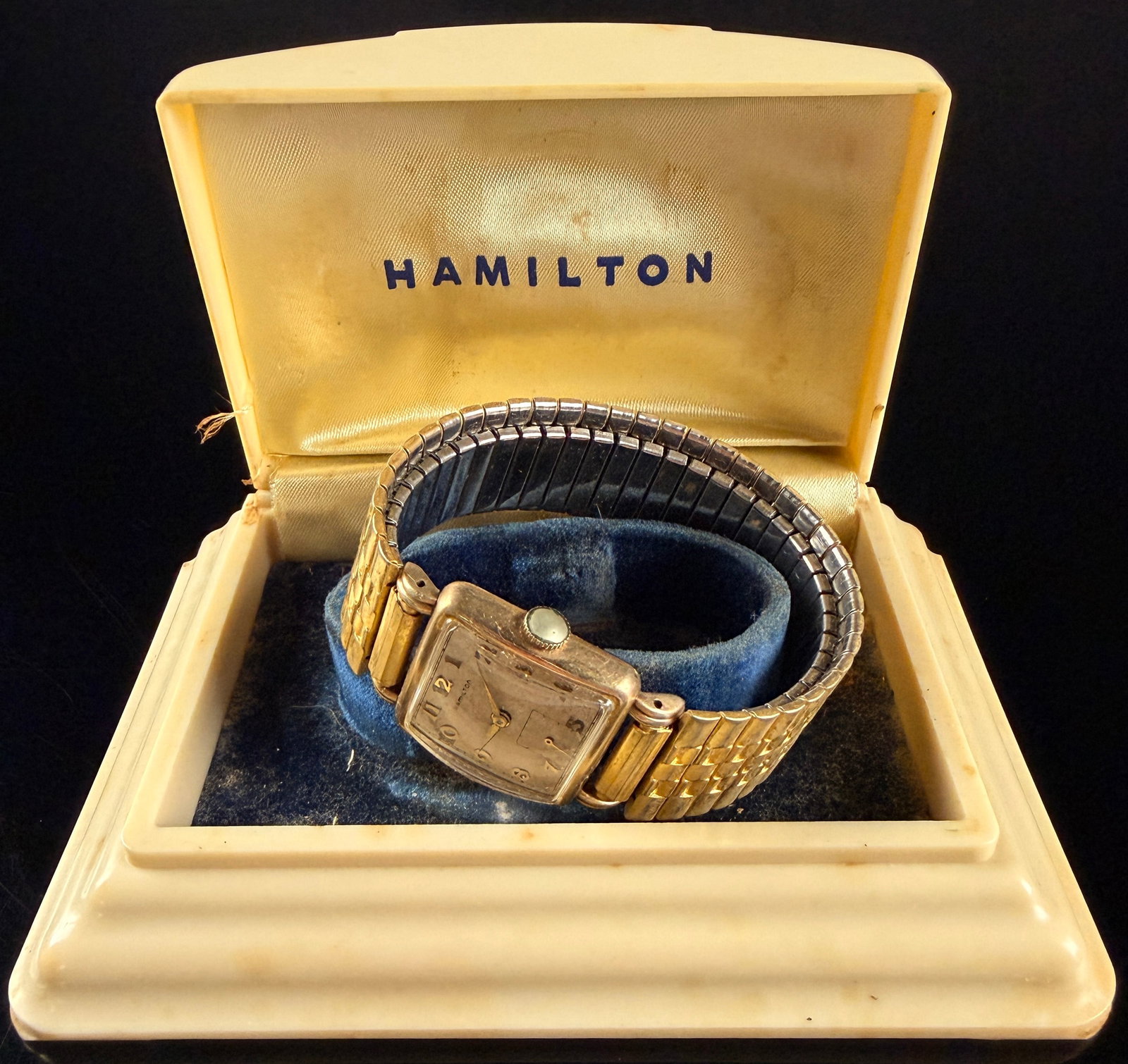 Vintage Hamilton Dewitt 10K Gold Filled Manual Wind Wristwatch with Original Box Runs: A vintage Hamilton Dewitt model men's wristwatch featuring a rectangular 10K gold filled tank style case. The cream dial displays applied gold tone Arabic numerals, a peripheral railroad minute track,