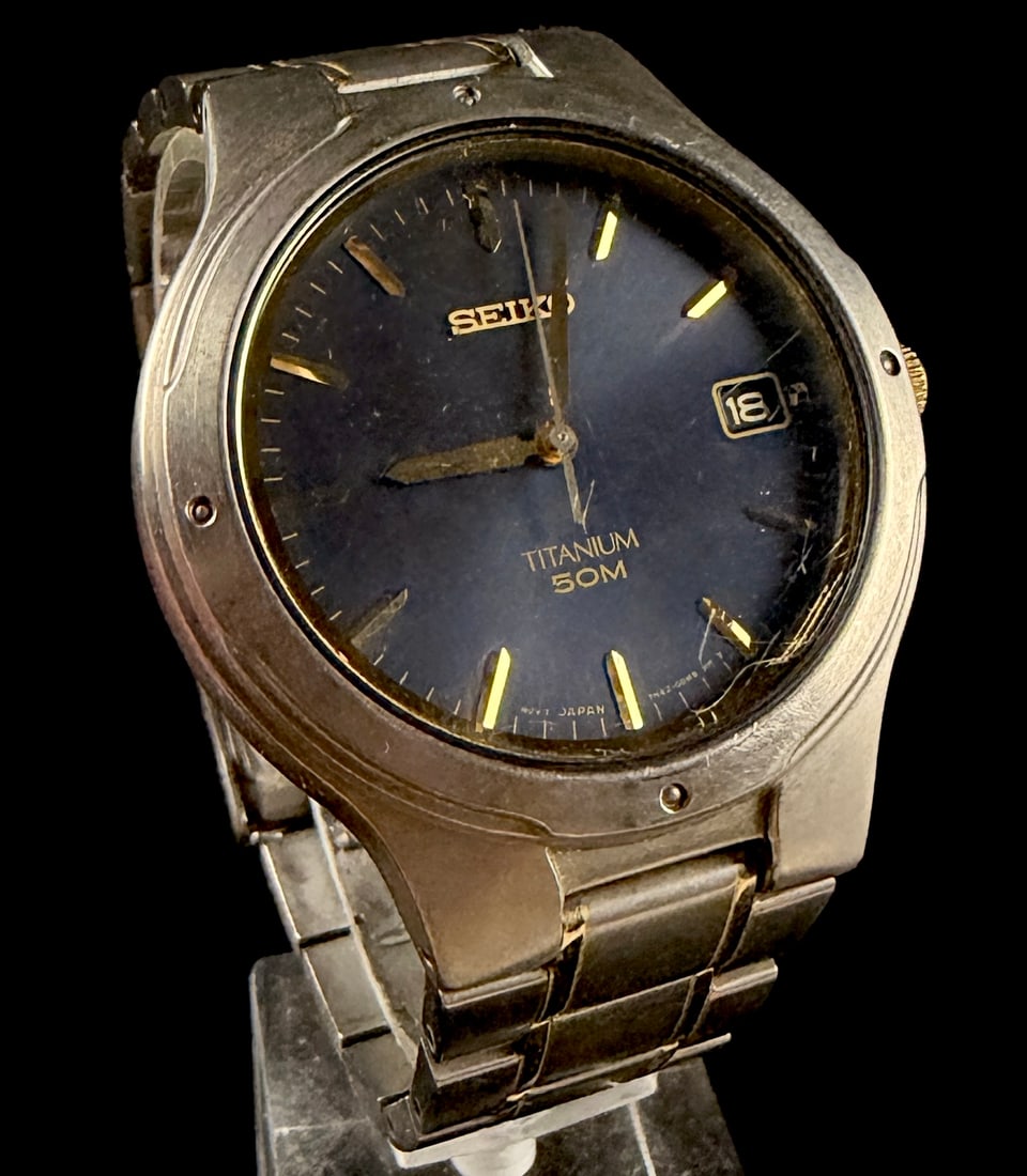 Seiko Titanium 50M Quartz Date Wristwatch, Reference 7N42-0BX0: A Seiko Titanium 50M wristwatch featuring a lightweight titanium case and integrated two-tone bracelet with gold-tone accents. The watch is powered by a Seiko Caliber 7N42 quartz movement. The dark bl