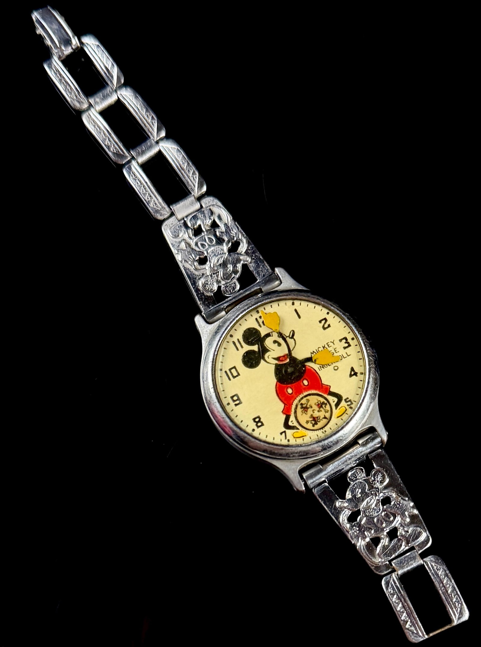 Vintage Ingersoll Mickey Mouse Manual Wind Wristwatch with Character Link Bracelet: A vintage Ingersoll Mickey Mouse wristwatch, dating to the mid-1930s. The cream-colored dial features an animated Mickey Mouse whose articulated arms serve as the hour and minute hands. At the 6 o'clo