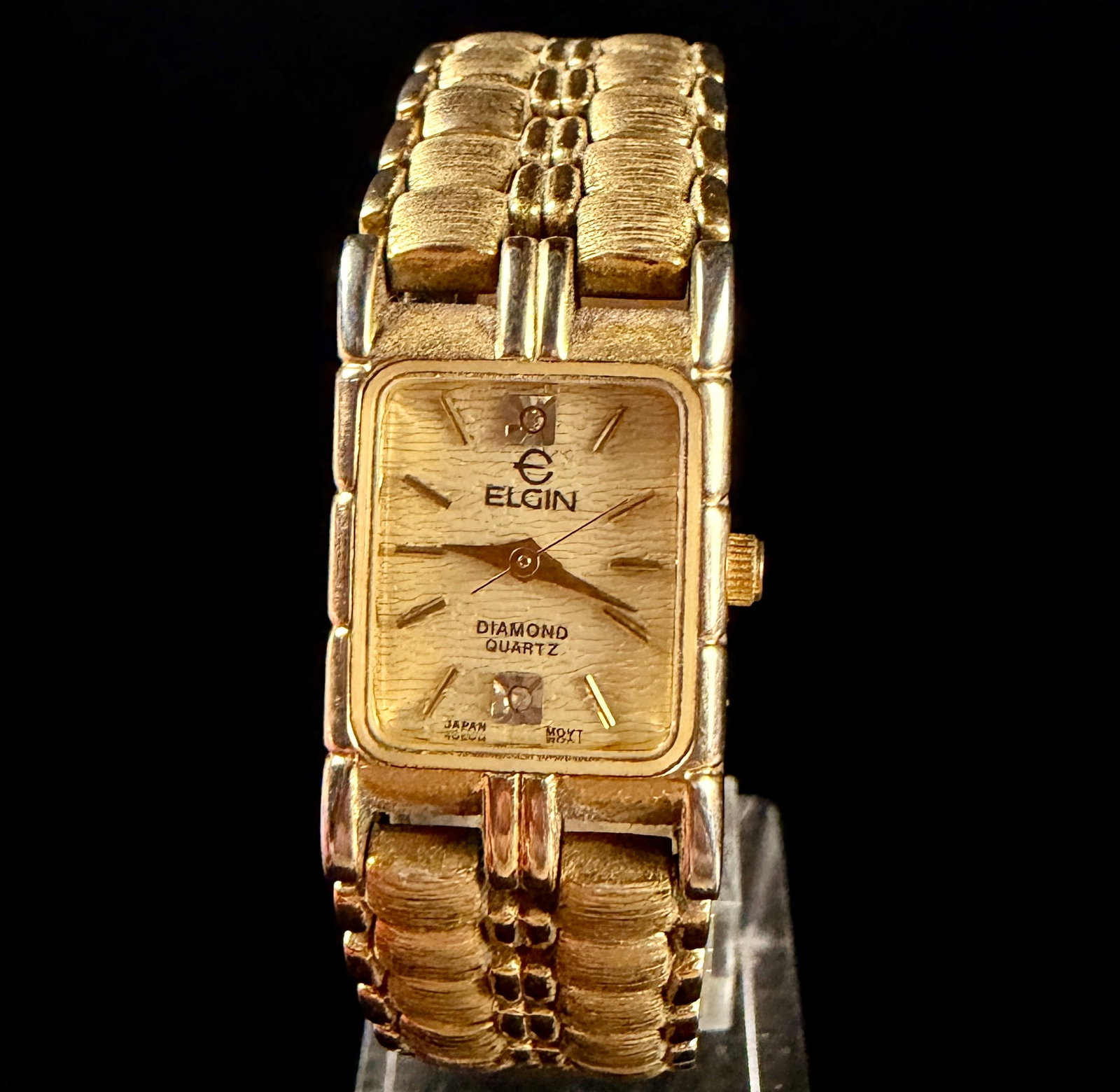 Elgin Diamond Quartz Ladies Tank Watch Gold Tone EM846: A ladies dress watch from Elgin, model Diamond Quartz, reference number EM846. The watch features a rectangular gold-toned base metal case and a gold-toned dial with a textured bark finish. The dial d
