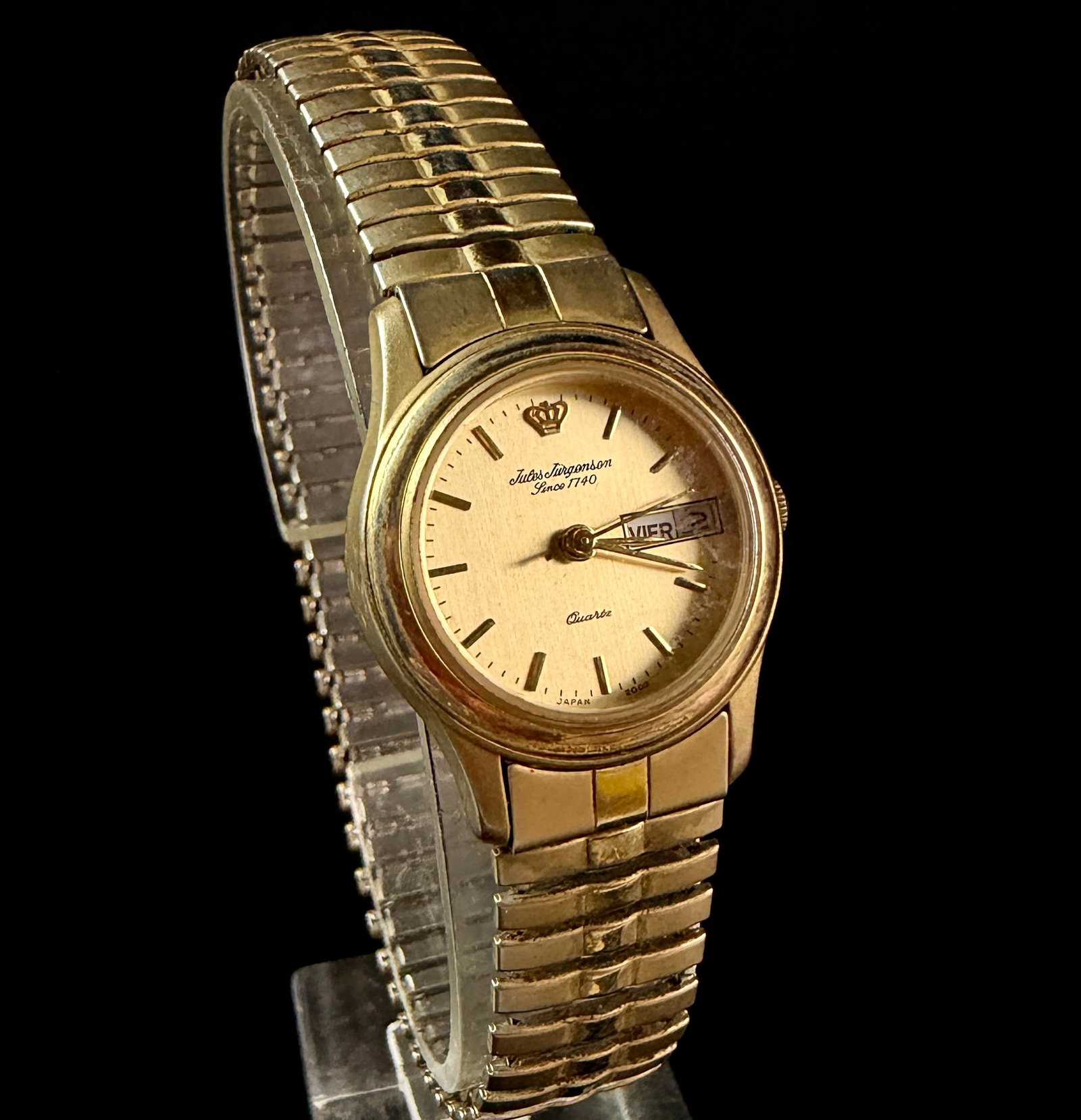 Jules Jurgensen Ladies Gold Tone Quartz Day Date Wristwatch Reference 3248: A vintage Jules Jurgensen ladies' wristwatch featuring a champagne-tone dial with gold-tone baton hour markers and a crown logo at the 12 o'clock position. The dial is printed with Jules Jurgensen, Si
