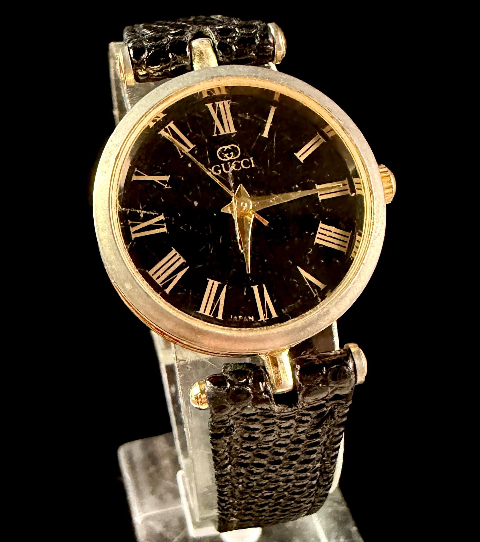 Gucci Vintage Gold-Toned and Red Enamel Ladies Wristwatch: This vintage ladies Gucci wristwatch features a round case crafted from gold-toned base metal accented with a red enamel-style stripe around the side. The black dial presents gold-toned Roman numeral 