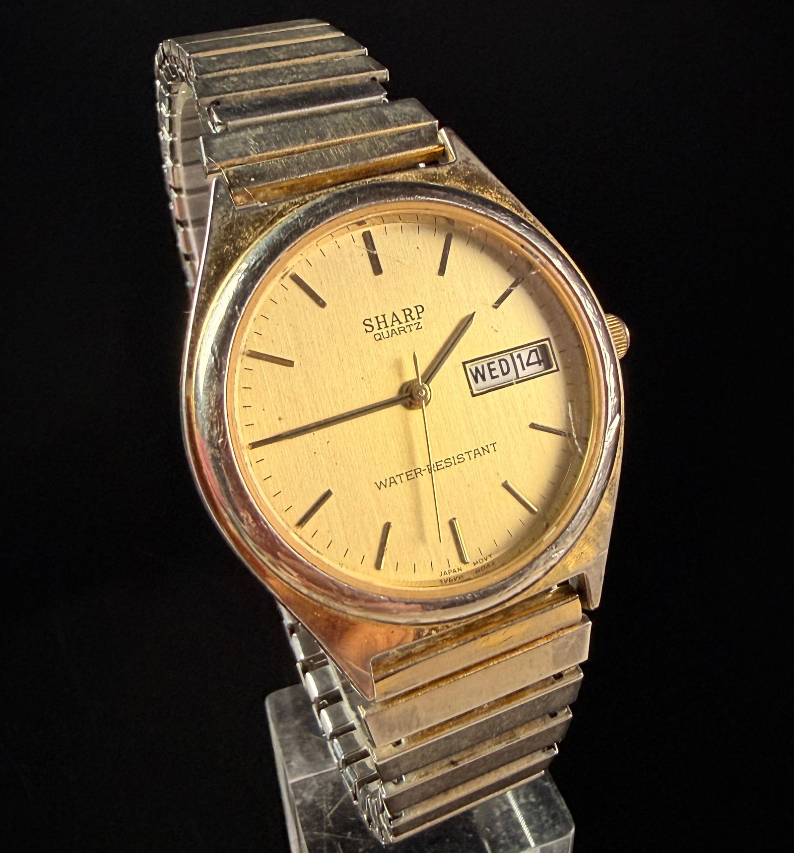 Sharp Quartz Day-Date Dress Watch with Two-Tone Expansion Bracelet: A vintage Sharp analog dress watch featuring a Japanese quartz movement. The watch is designed with a champagne-colored dial exhibiting a vertical brushed finish, gold-tone baton hour markers, and a d