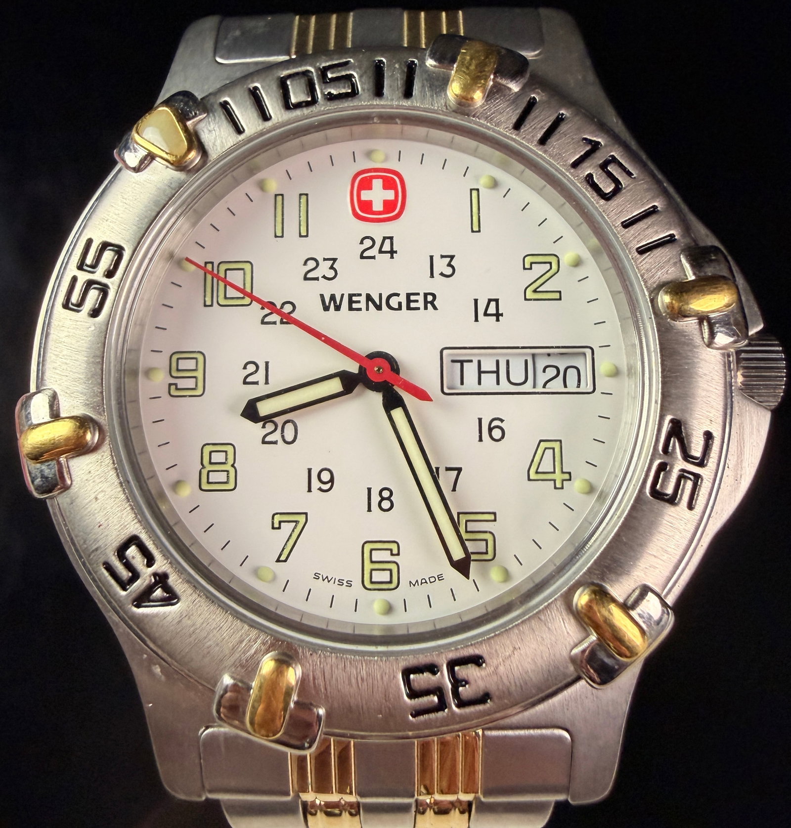 Wenger Swiss Military Two-Tone Day-Date Wristwatch Ref 096.0685: Wenger Swiss Military quartz wristwatch, reference 096.0685. The timepiece features a brushed stainless steel case accented by a gold-tone finished bezel and crown. The white dial is detailed with lum