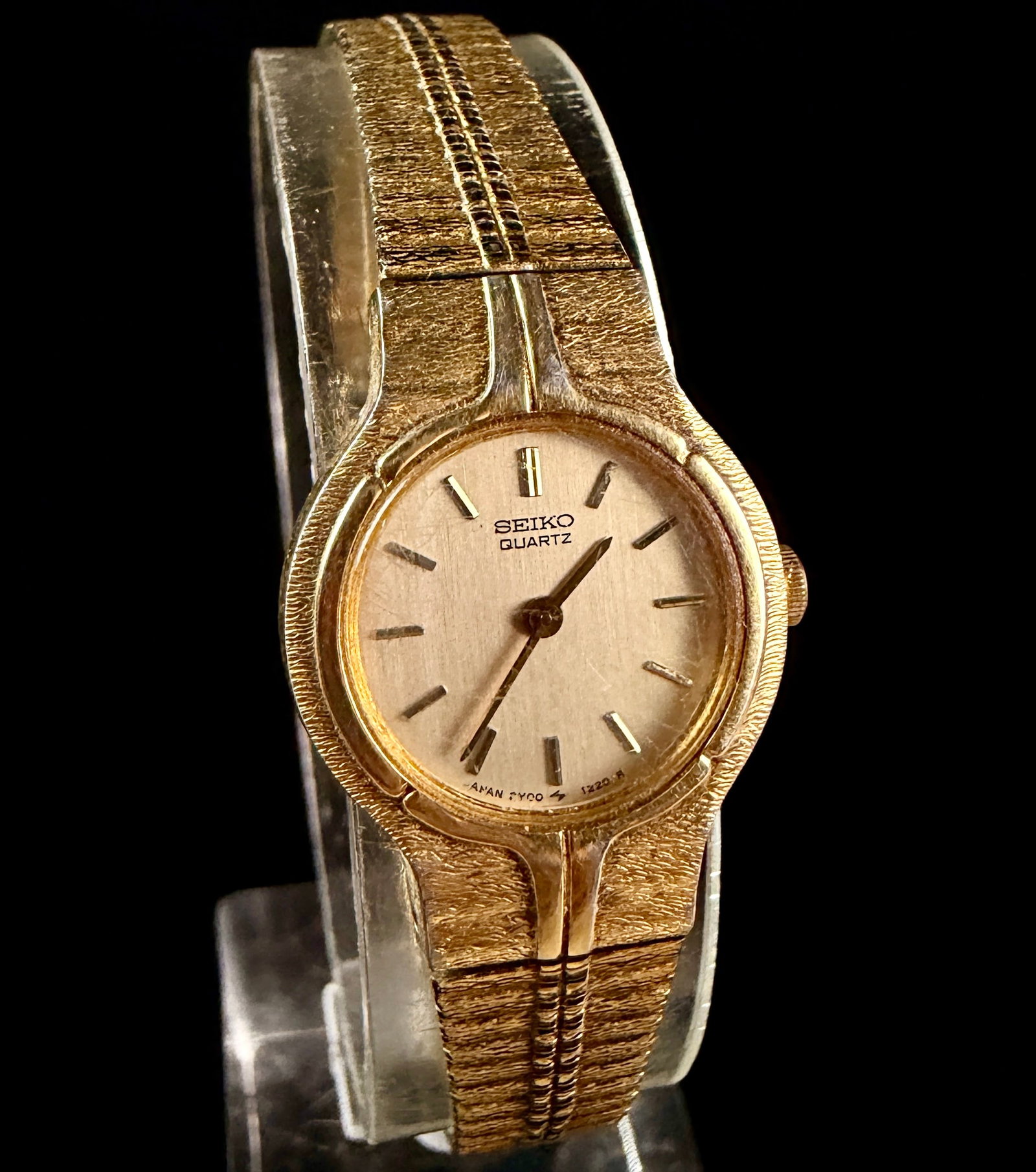 Seiko Ladies Quartz Wristwatch Reference 2Y00-0189: A vintage Seiko ladies quartz wristwatch featuring an integrated gold-tone base metal bracelet with a bark-textured finish and a central double-ridged motif. The watch has a circular champagne-toned d