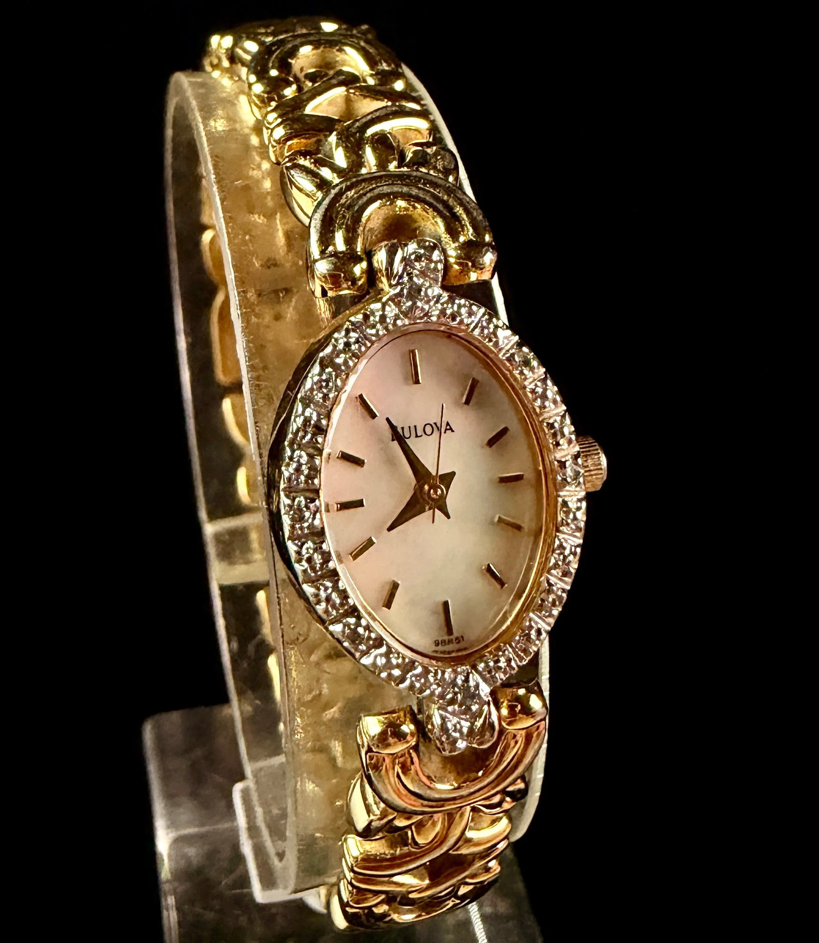 Bulova Ladies Diamond Collection Quartz Dress Watch Reference 98R51: Bulova Ladies Diamond Collection quartz dress watch, reference number 98R51. The timepiece features an oval case with a gold-tone base metal bezel set with diamond accents. The dial is composed of iri
