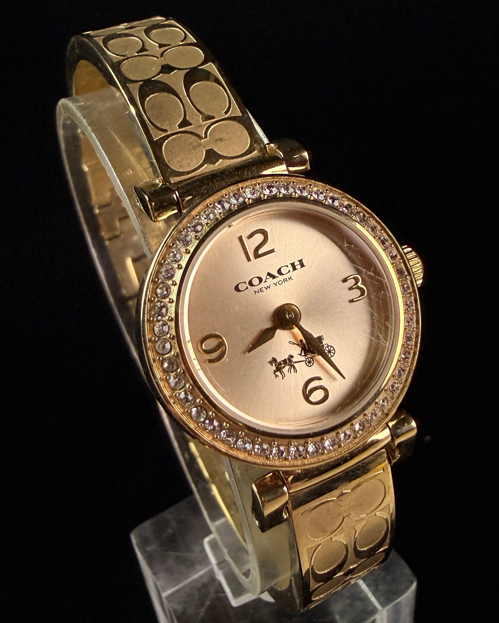 Coach Madison Signature Gold-Tone Crystal Bangle Watch CA.72.7.34.0992S: This Coach Madison Signature bangle watch features a gold-toned stainless steel construction with an integrated bracelet. The round case is encircled by a bezel set with a single row of round clear cr