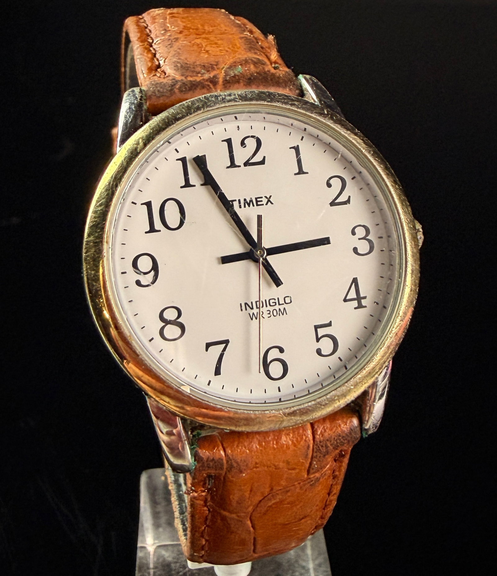 Timex Indiglo Easy Reader Gold-Tone Quartz Wristwatch: A vintage Timex Indiglo Easy Reader style quartz wristwatch. The timepiece features a round gold-tone base metal case with a stainless steel snap-on case back. The off-white dial is detailed with larg