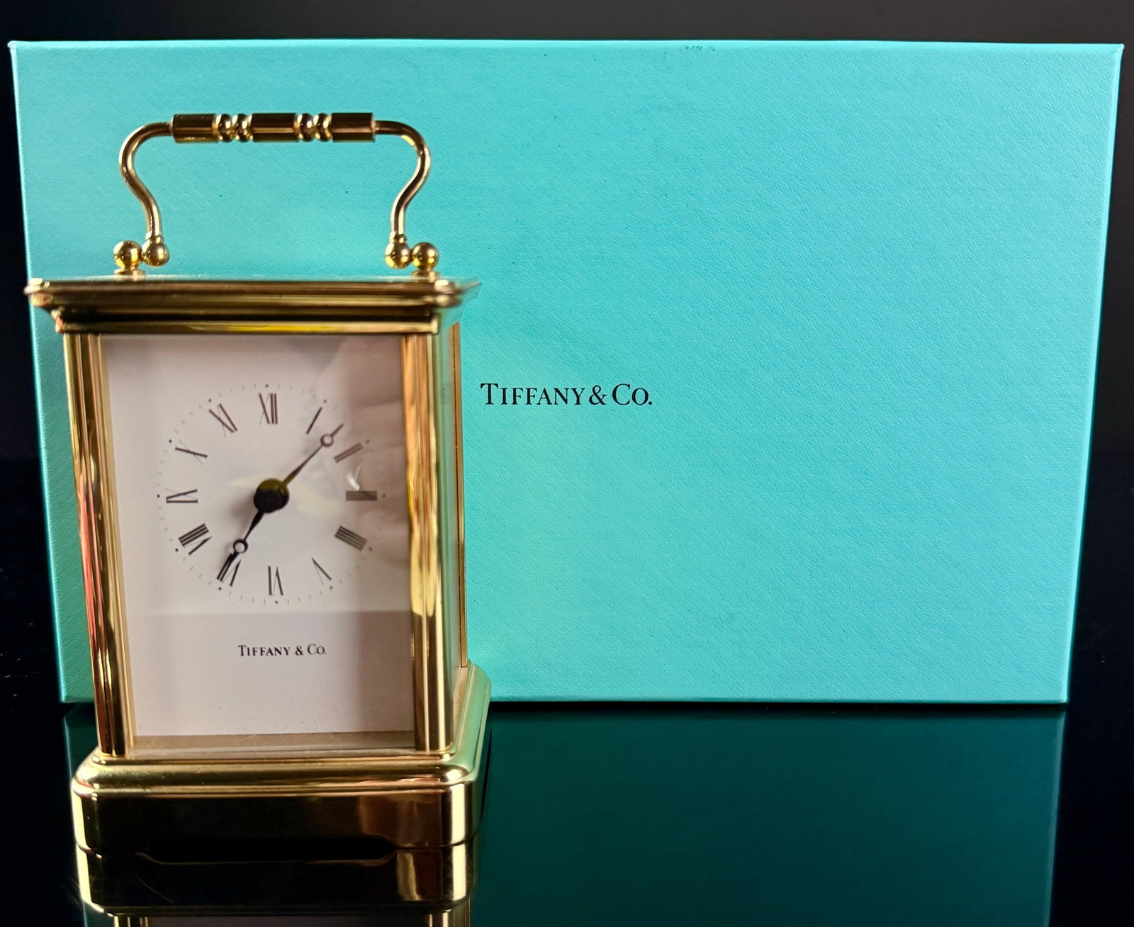 Tiffany & Co. Brass Quartz Carriage Clock with Presentation Box: A brass carriage clock retailed by Tiffany & Co. with a German-manufactured quartz movement. The rectangular case features a combination of polished and brushed brass finishes, a top-mounted swing car