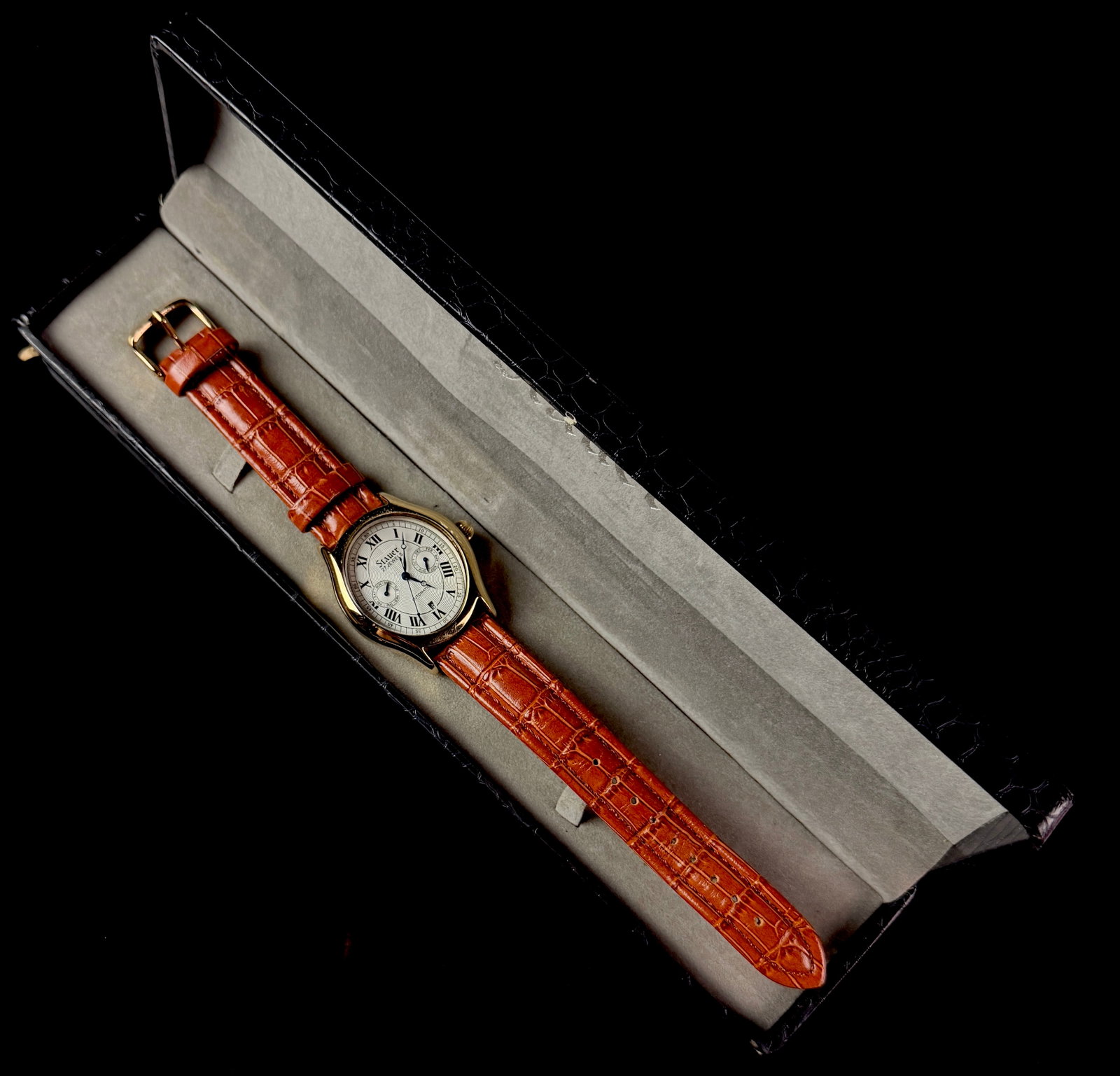 Stauer Model 13871 Gold Tone Automatic Wristwatch with Presentation Box: Stauer model 13871 wristwatch featuring a gold-tone stainless steel case and a cream-colored guilloche dial. Materials for this lot include stainless steel, leather, and the item needs a battery. The 