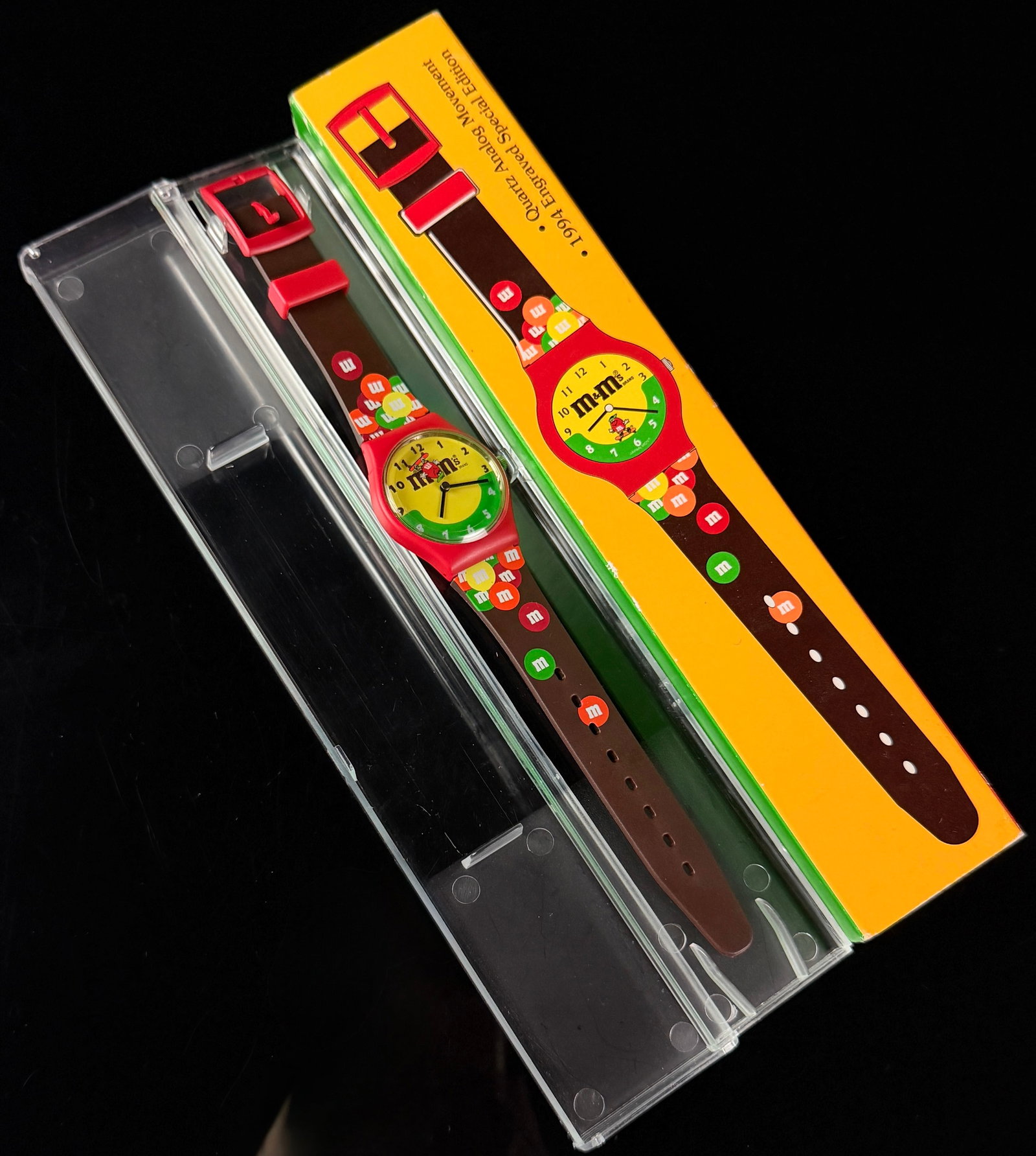 M&M's 1994 Engraved Special Edition Quartz Analog Wristwatch: M&M's branded 1994 Engraved Special Edition quartz analog wristwatch produced for Mars, Inc. The watch features a red plastic case and a bi-color yellow and green dial. The dial is printed with the bl