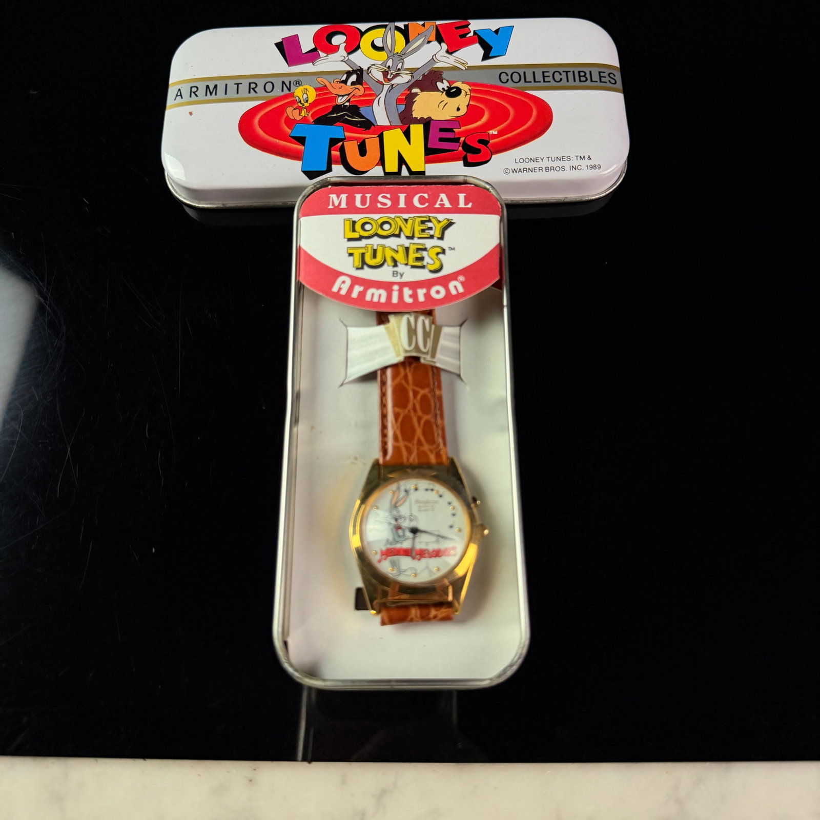 Armitron Looney Tunes Merrie Melodies Musical Quartz Gold-Tone Watch with Original Tin 32mm: This is a vintage 1989 Armitron Looney Tunes collectible musical quartz wristwatch featuring a Merrie Melodies motif. The gold-tone base metal case houses a white dial illustrated with Bugs Bunny dres