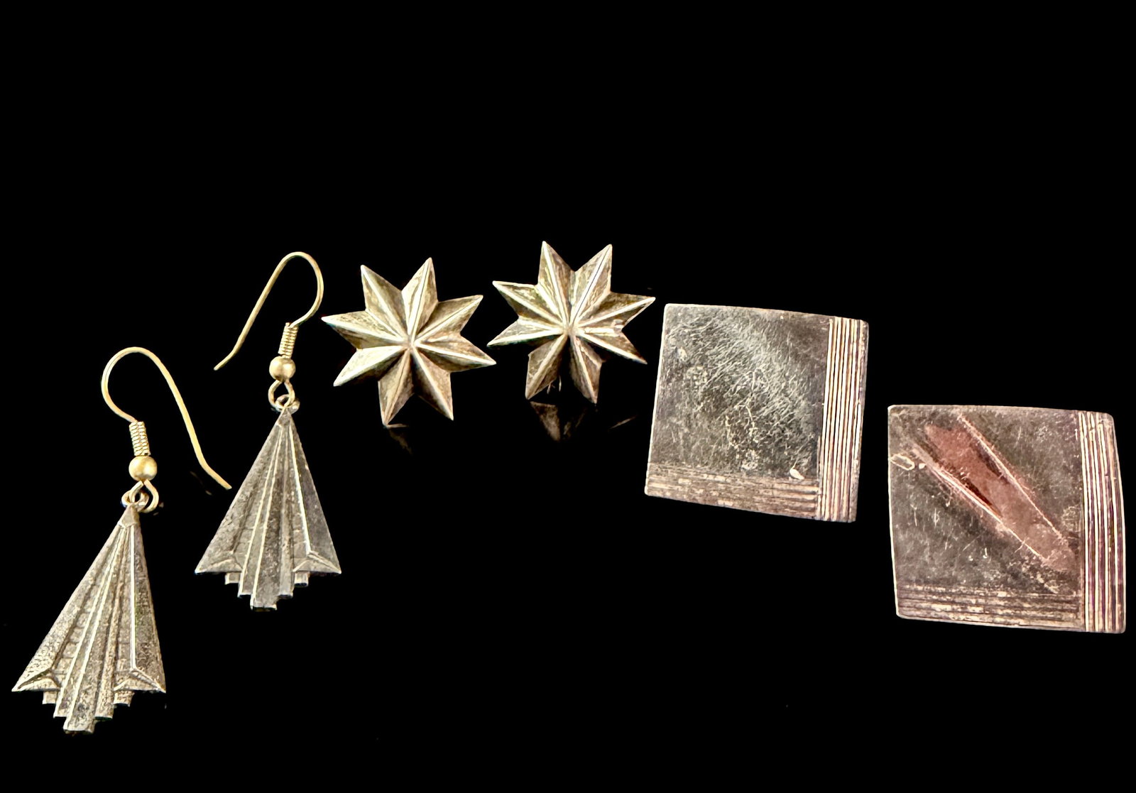 A Trio of Matched Pairs of Sterling Silver Earrings including Tahe Navajo Drop Earrings: This lot comprises three matched pairs of sterling silver earrings. The first pair consists of Navajo drop earrings with a geometric, fan-shaped design featuring a tiered, stepped lower edge and