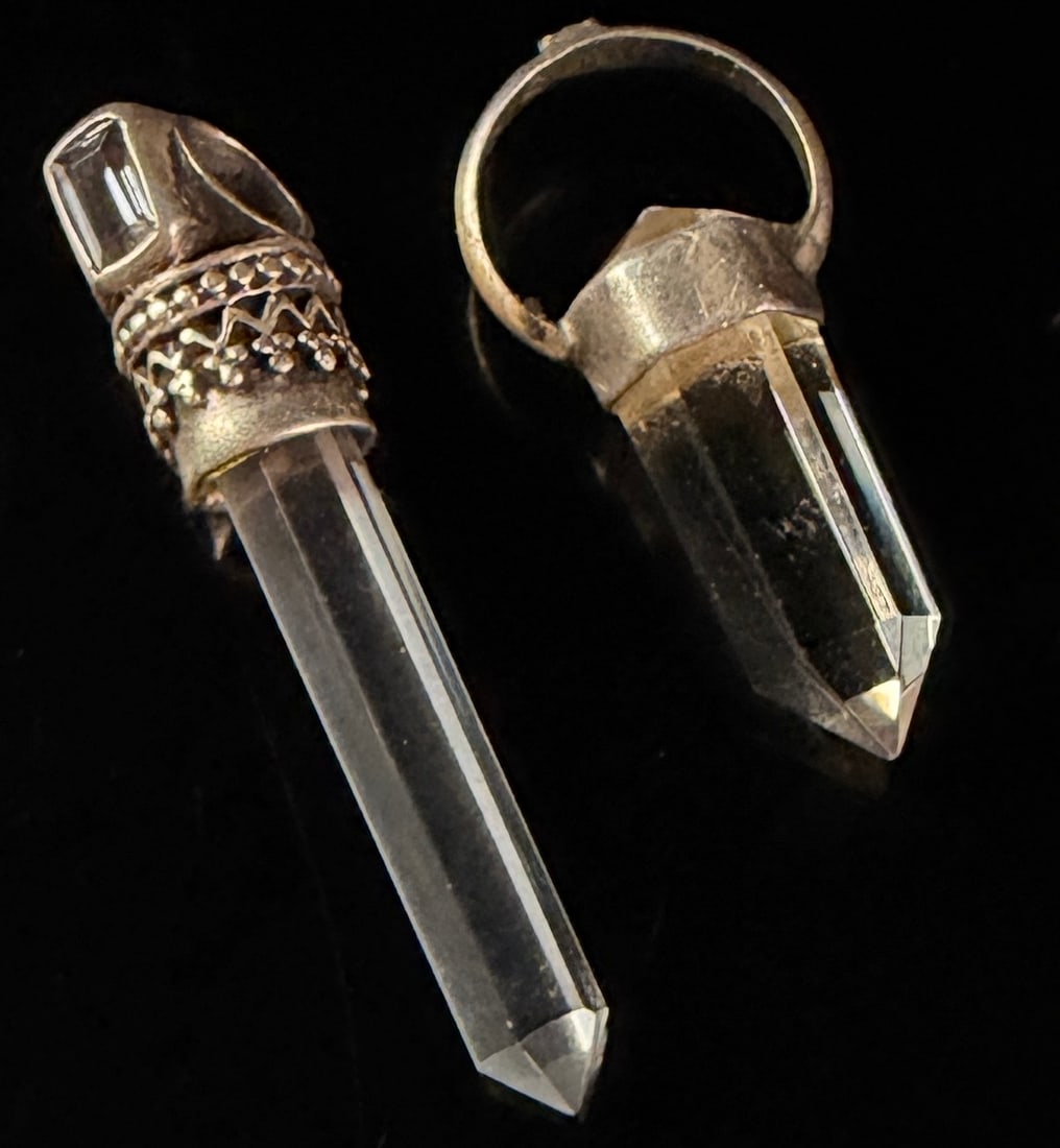 Two Clear Quartz Crystal Point Pendants with Silver-Toned Metal Mounts: Two clear quartz crystal point pendants. The first pendant consists of a long clear hexagonal-cut quartz crystal point mounted in a silver-toned metal cap. The cap features ornate filigree-style scrol