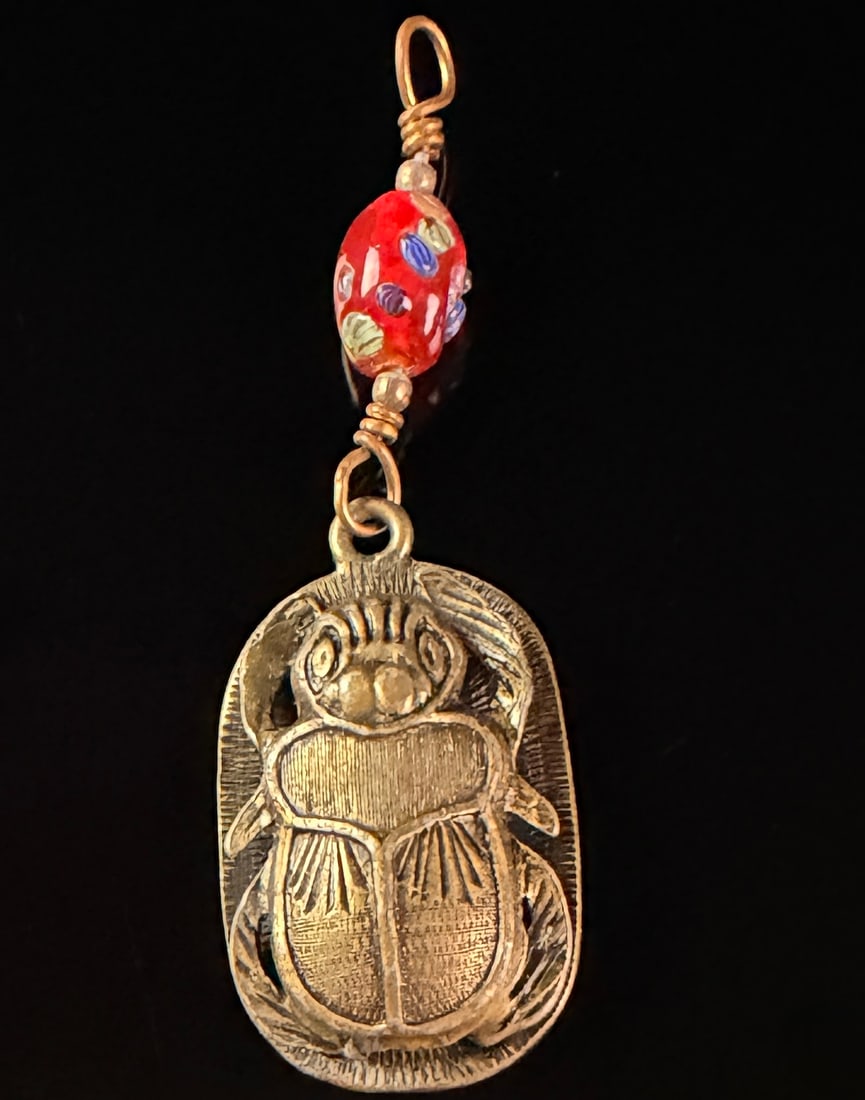 Egyptian Revival Cast Metal Scarab Pendant with Lampwork Glass Bead: An Egyptian Revival-style scarab pendant charm. The piece is constructed from cast base metal with an antiqued gold-toned finish. The obverse features a relief-cast stylized scarab beetle on a texture
