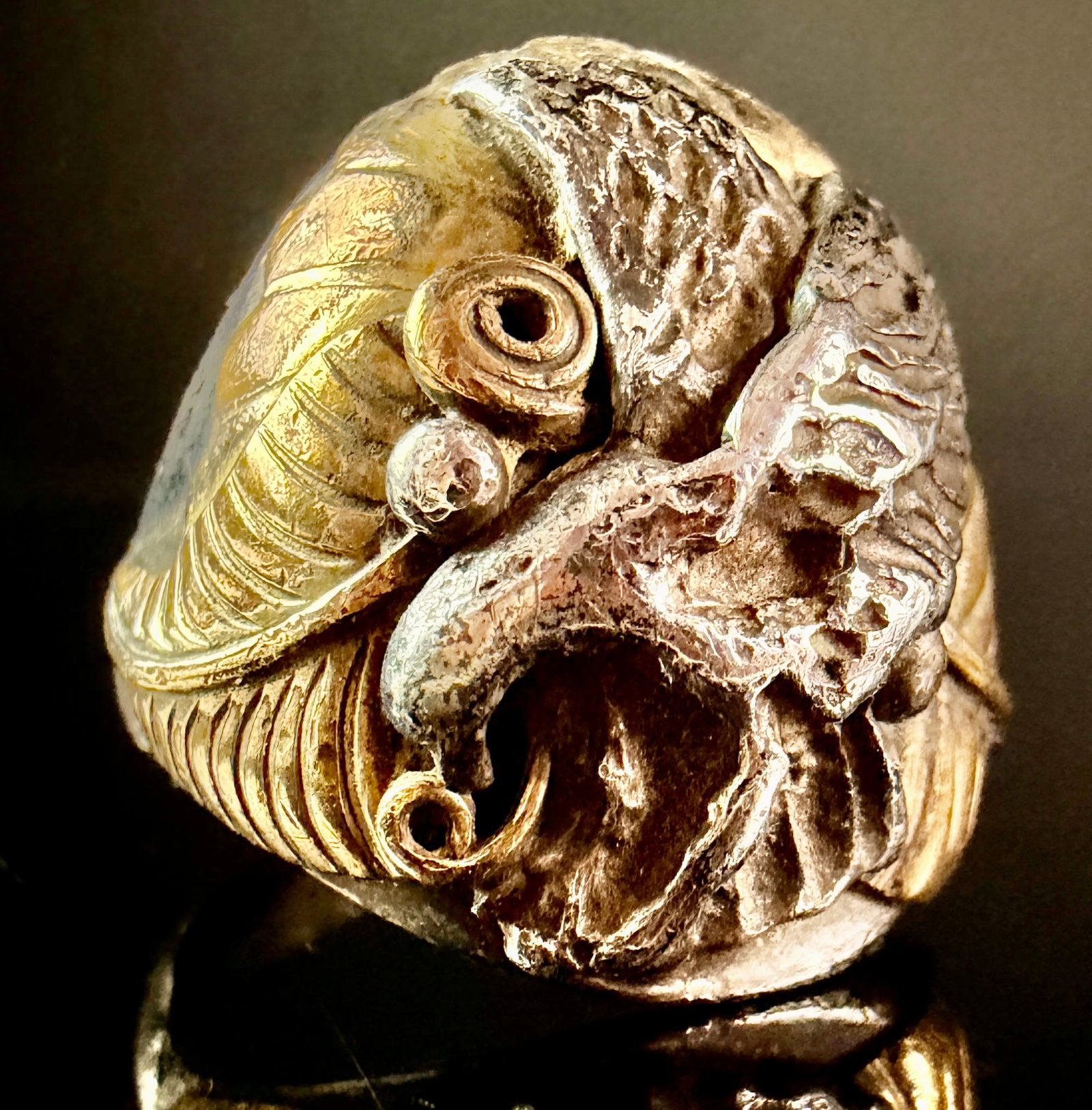 Two-Tone Metal Sculptural Eagle Statement Ring: A large sculptural statement ring featuring a central eagle head in high relief, flanked by stylized textured wings that wrap around to form the shoulders of the band. The design utilizes two