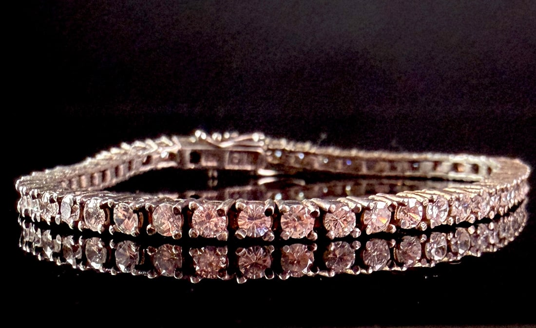 Sterling Silver Gold Tone Tennis Bracelet with Faceted Stones: A classic tennis style bracelet featuring a continuous line of round brilliant-cut clear faceted stones set in four-prong mounts. The bracelet is constructed from sterling silver with a yellow