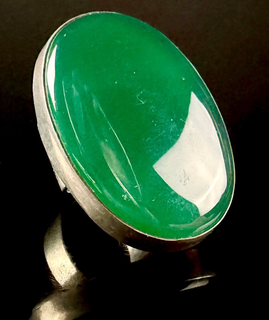 Sterling Silver and Chrysoprase Modernist Statement Ring: A modernist statement ring featuring a large high-domed oval cabochon of translucent vibrant green stone. The stone is secured in a sterling silver bezel setting mounted to a rectangular backplate