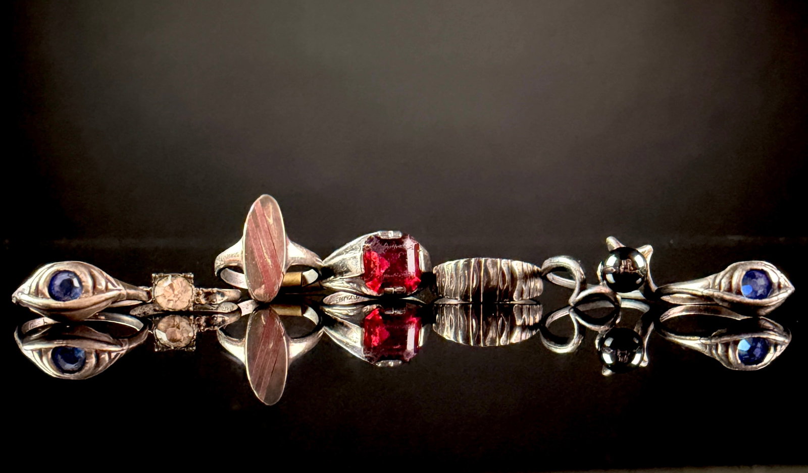 A Collection of Six Vintage and Modernist Sterling Silver and Gemstone Rings: A collection of six sterling silver rings featuring various stones and modernist designs. The assortment includes a sculptural bypass ring set with a dark metallic spherical bead, a wide band with a v